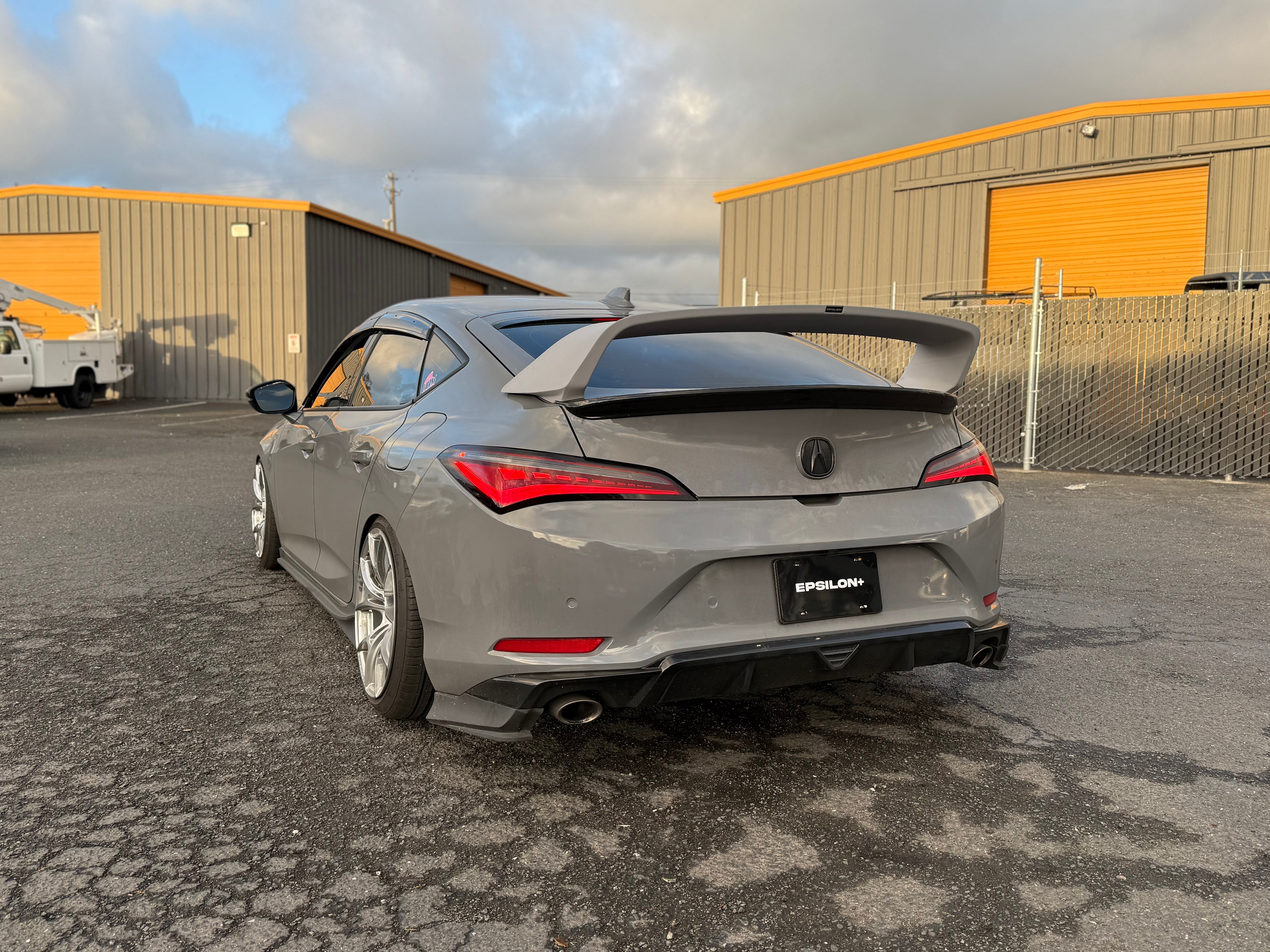 Rear three-quarter view of a silver Acura Integra with Sport Wing outside a warehouse