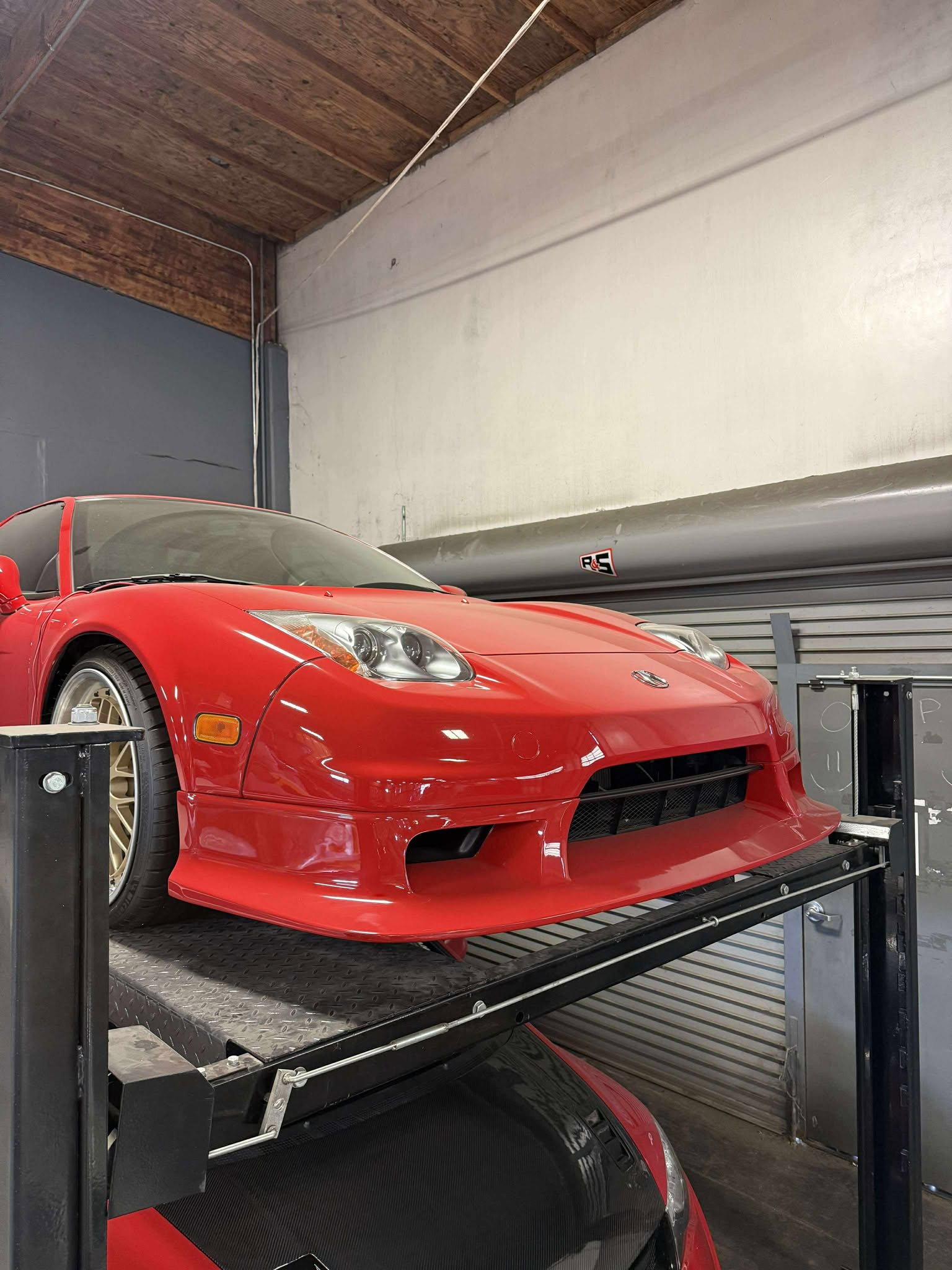 Red Acura NSX with the R-GT front lip fitted, raised on a garage lift