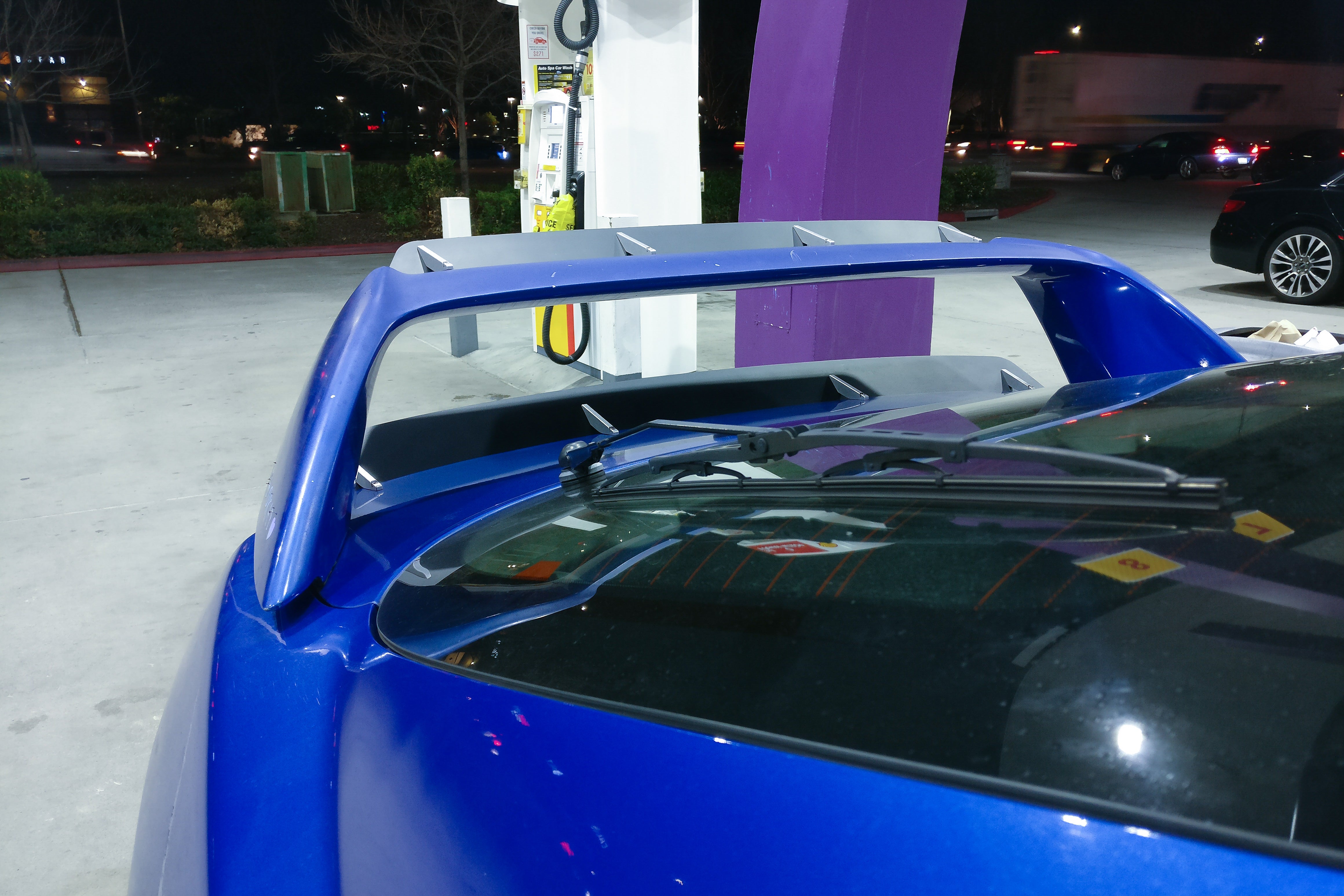 Front view of a blue Acura RSX showing the double spoiler extension at a gas station at night