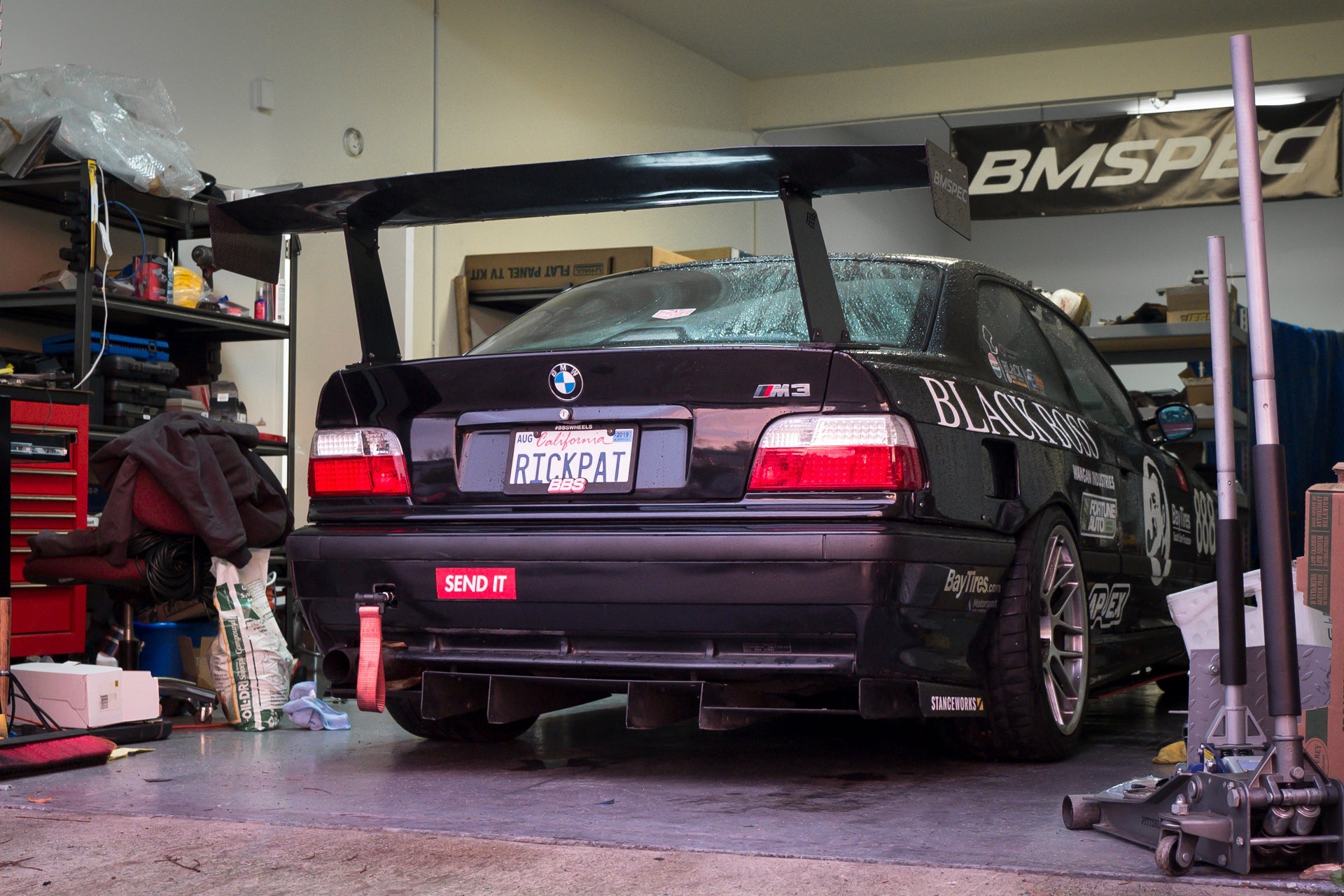 Rear three-quarter view of a black BMW E36 M3 motorsport car with GT wing in a garage