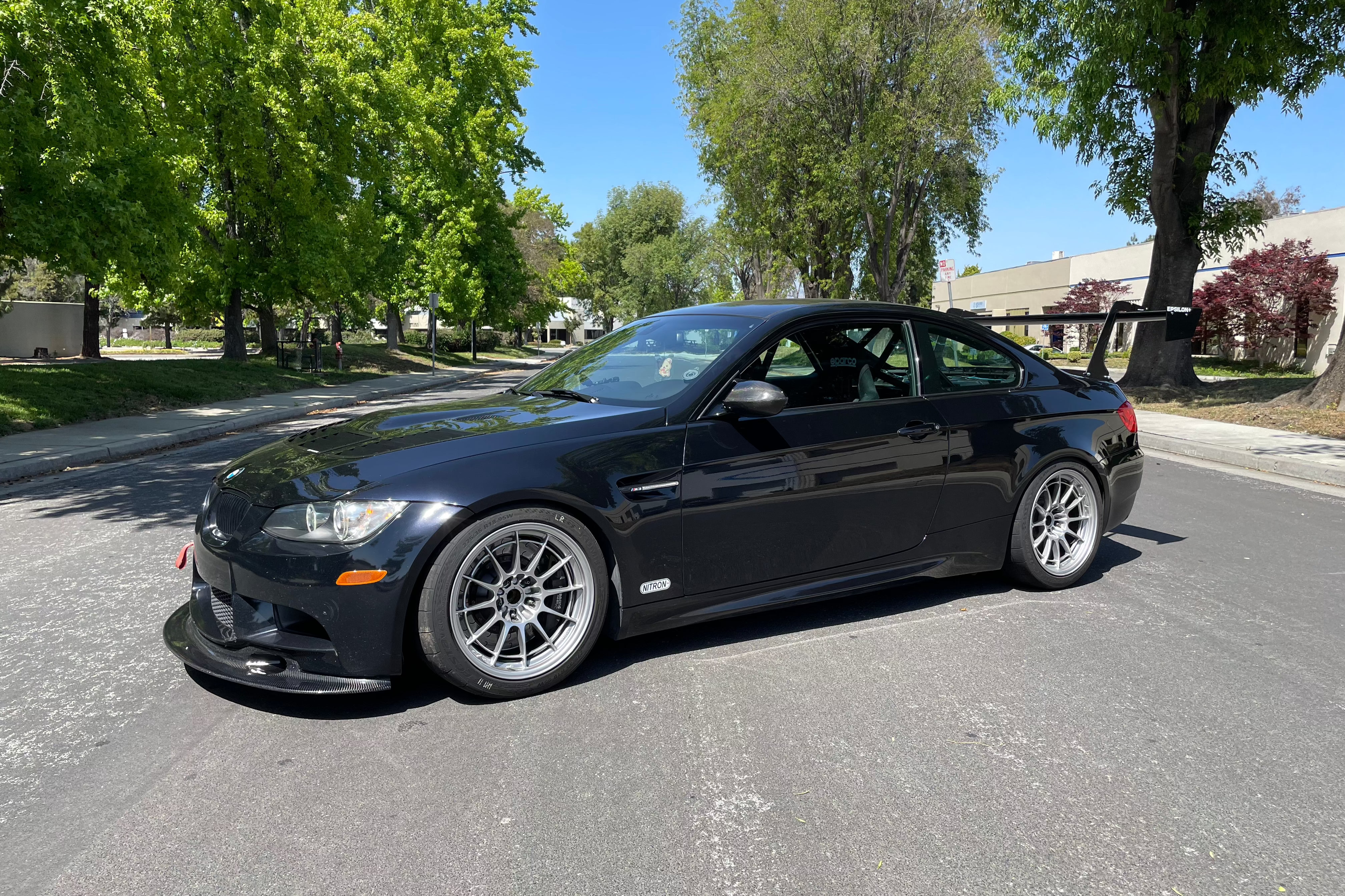 Black BMW E92 M3 with the Epsilon+ GT wing parked on a tree-lined street