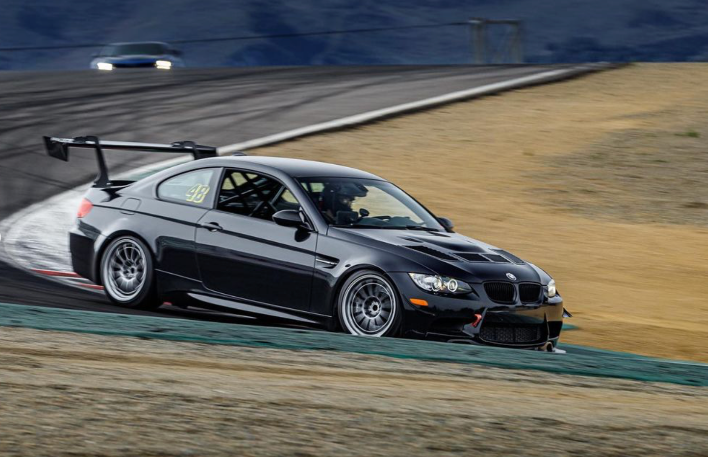 Rear three-quarter view of a black BMW E92 M3 with GT wing on track