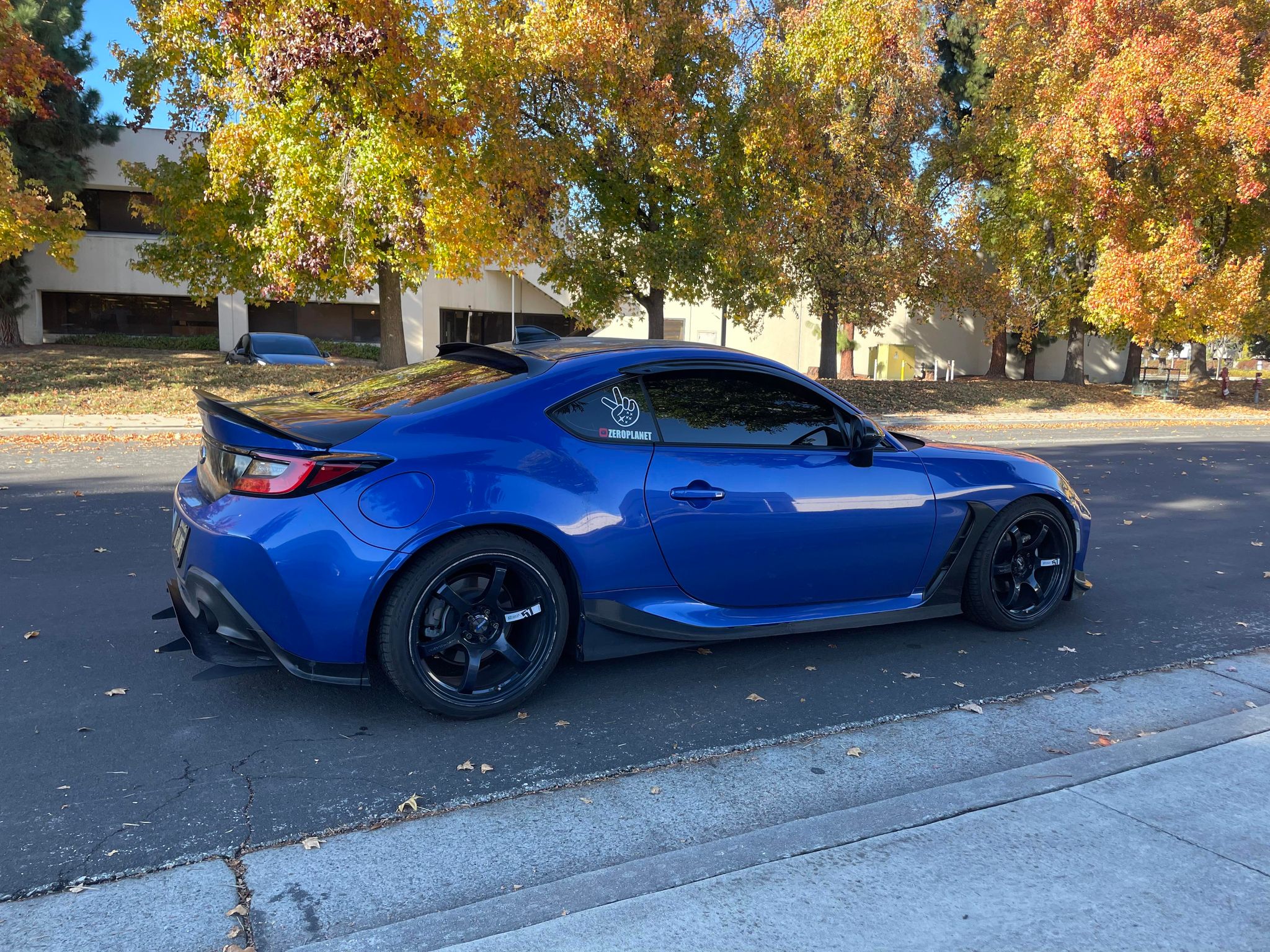 Rear three-quarter view of a blue Subaru BRZ ZN8 with side skirts on a tree-lined street