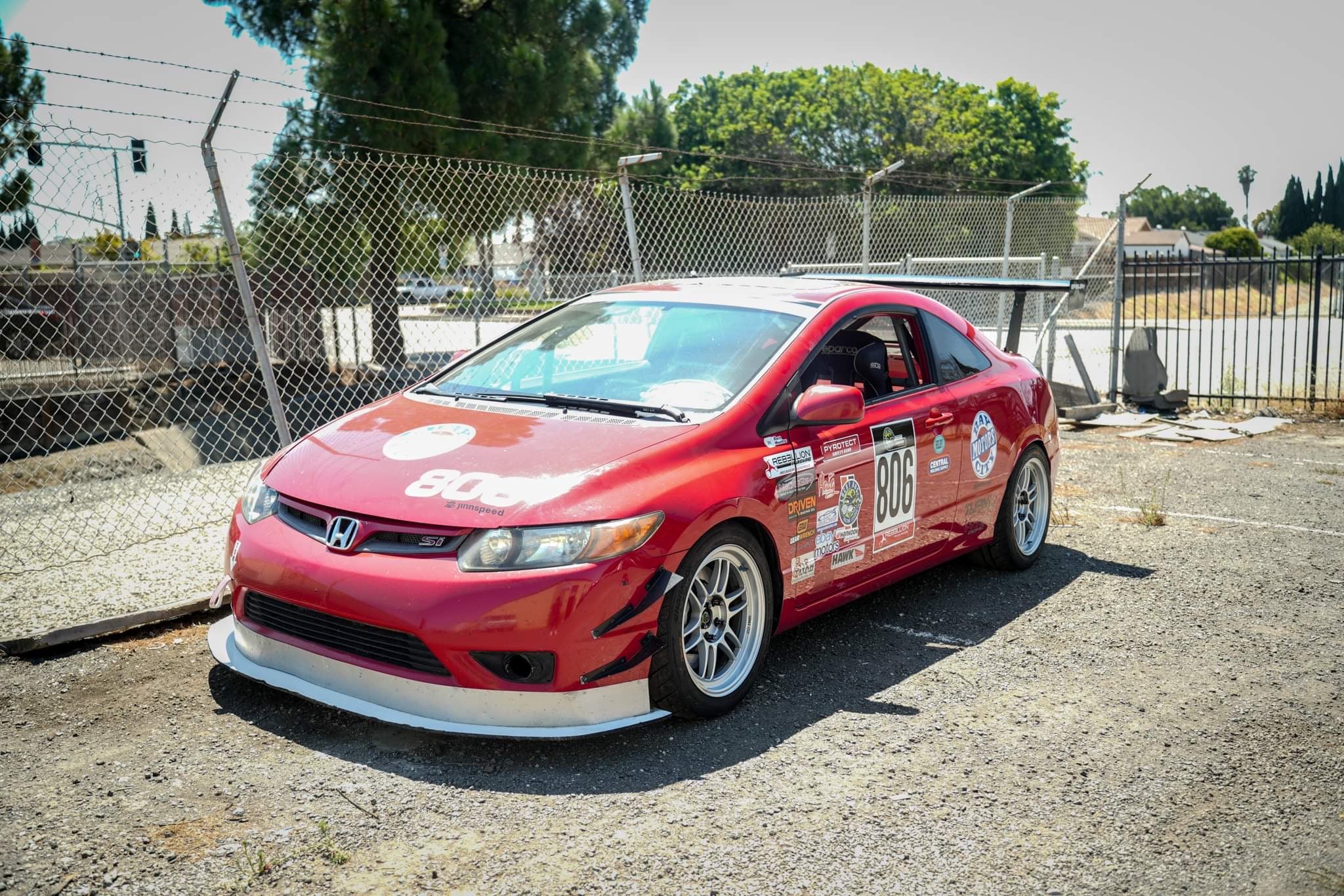 Front three-quarter view of a red Civic Coupe FG2 race car parked trackside with GT wing