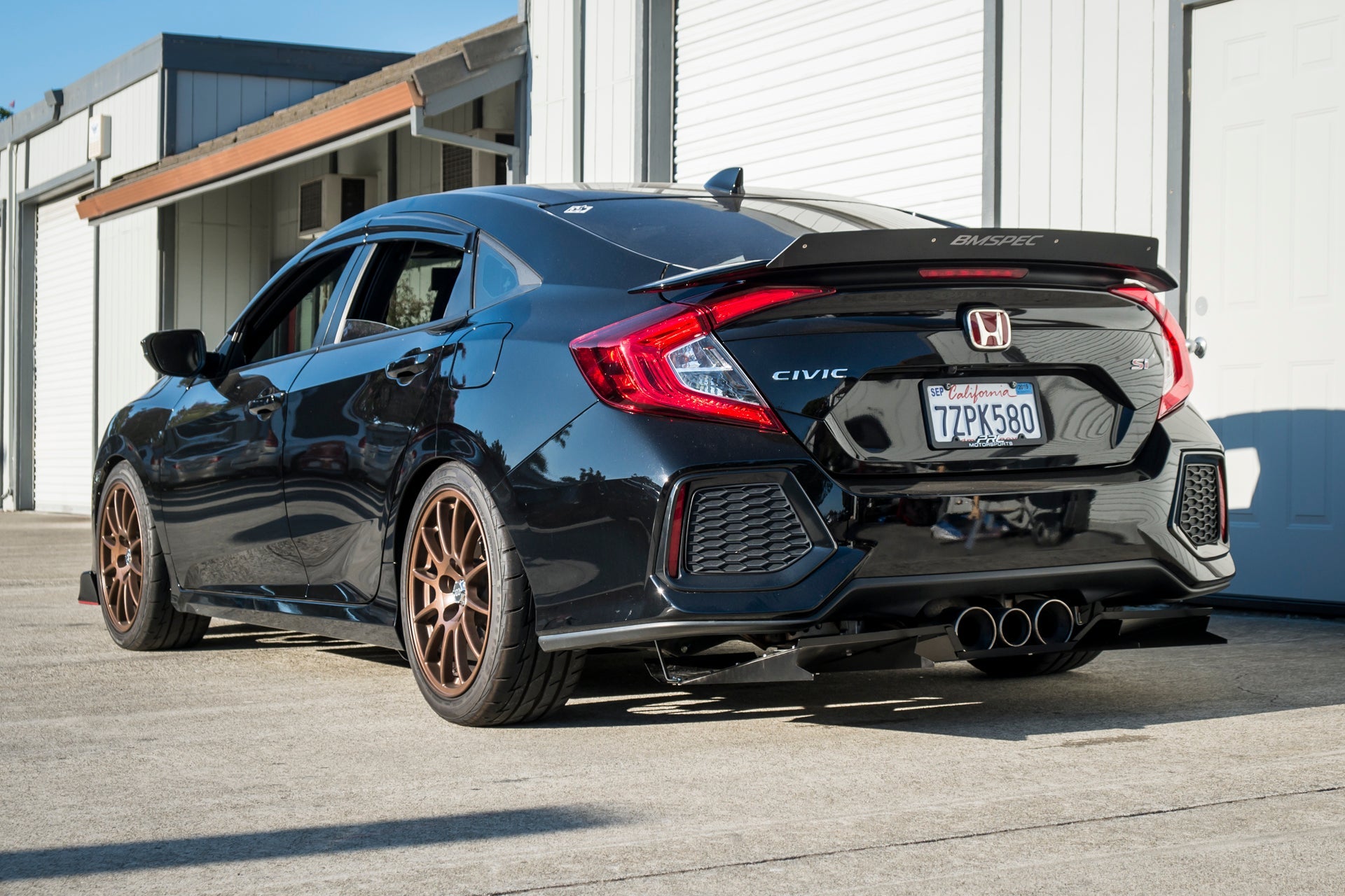 Rear three-quarter view of a black Civic Si Sedan with diffuser and bronze wheels