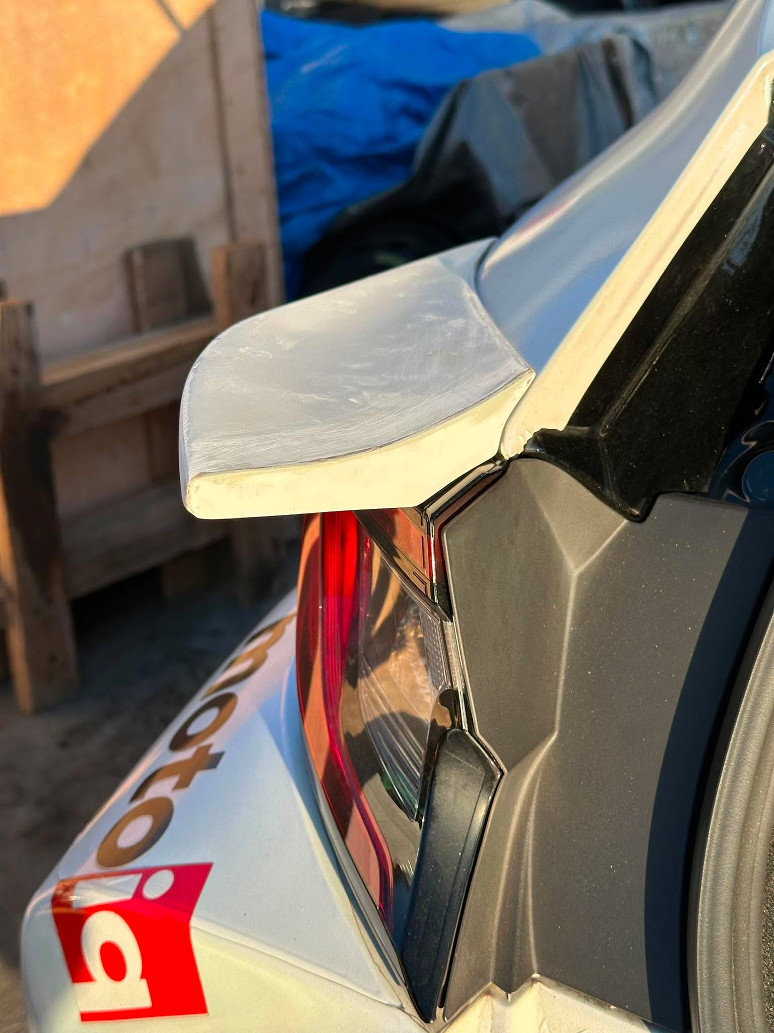 Unpainted Epsilon+ mid wing resting against a Corolla Hatchback during fitment