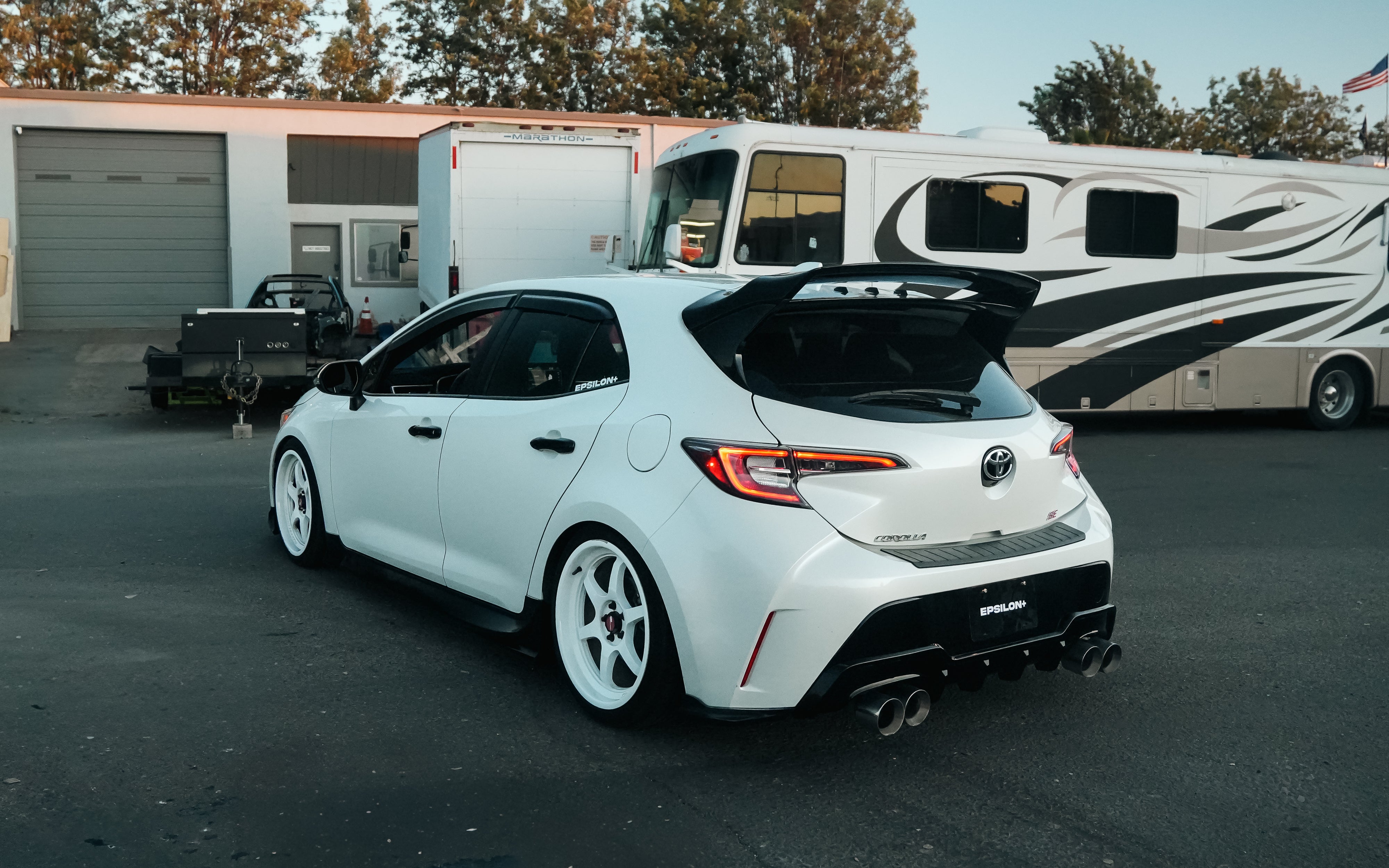 White Corolla Hatchback with rear spats parked beside a warehouse