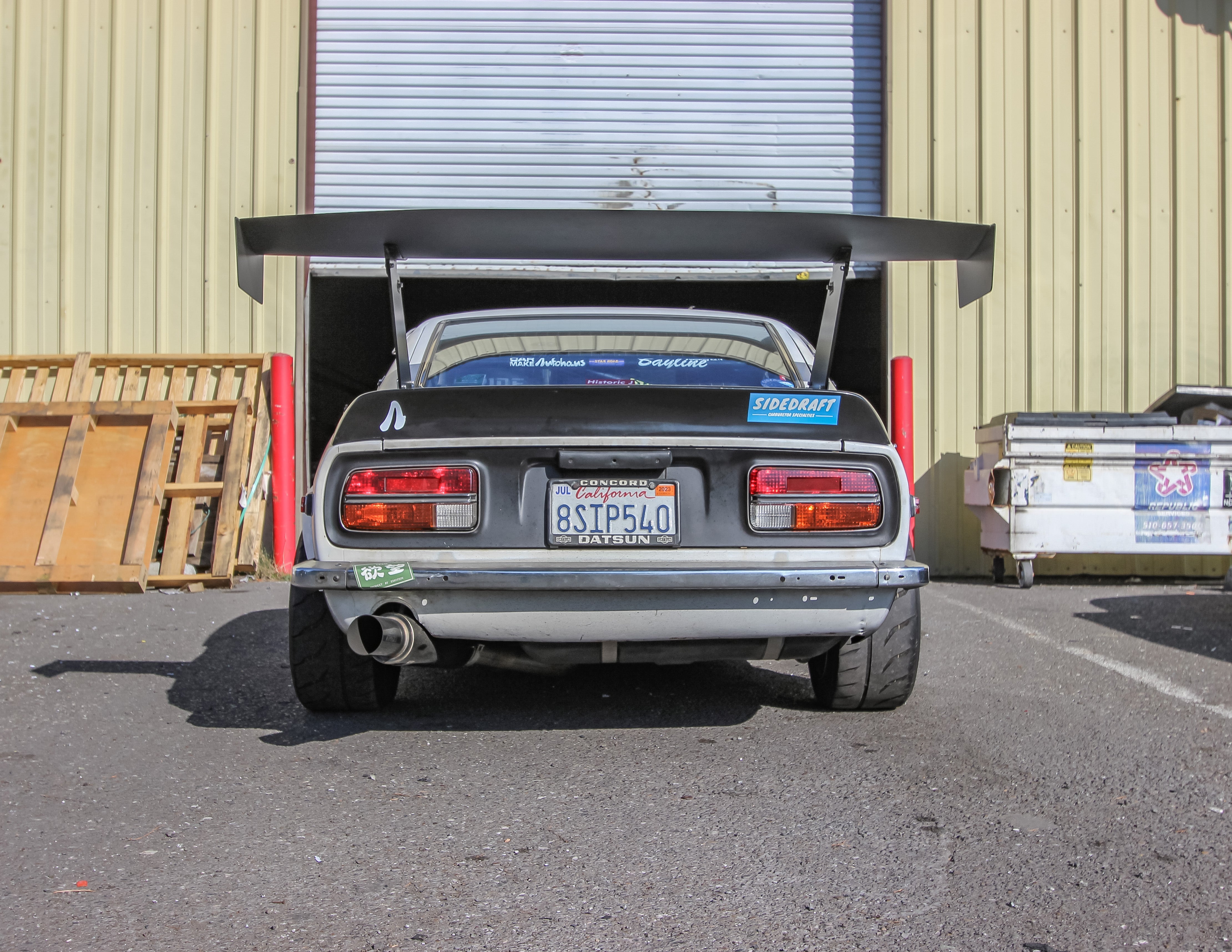 Rear view of a black Datsun 240Z with GT wing showing endplate branding