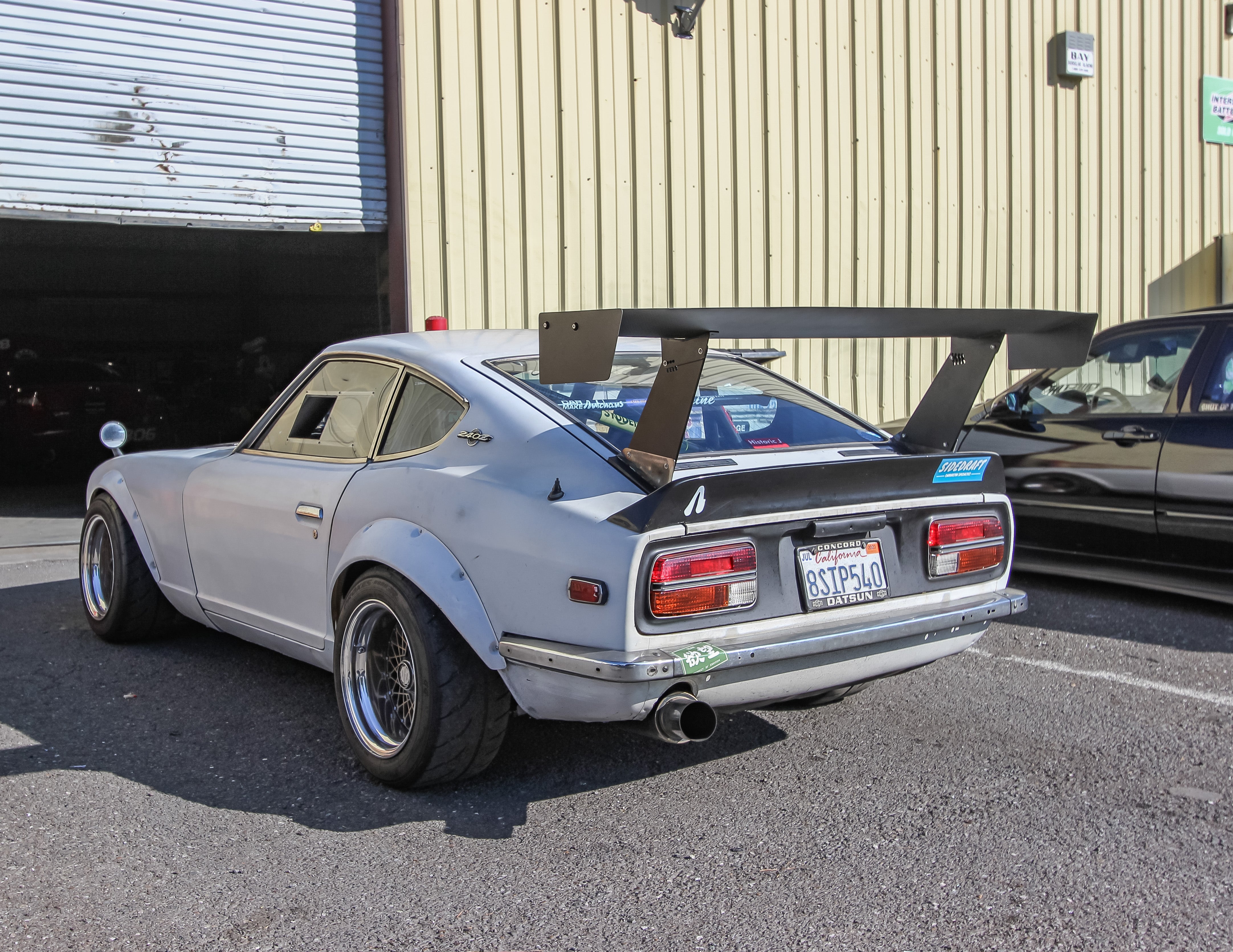 Side profile of a silver Datsun 240Z with GT wing parked outside a warehouse