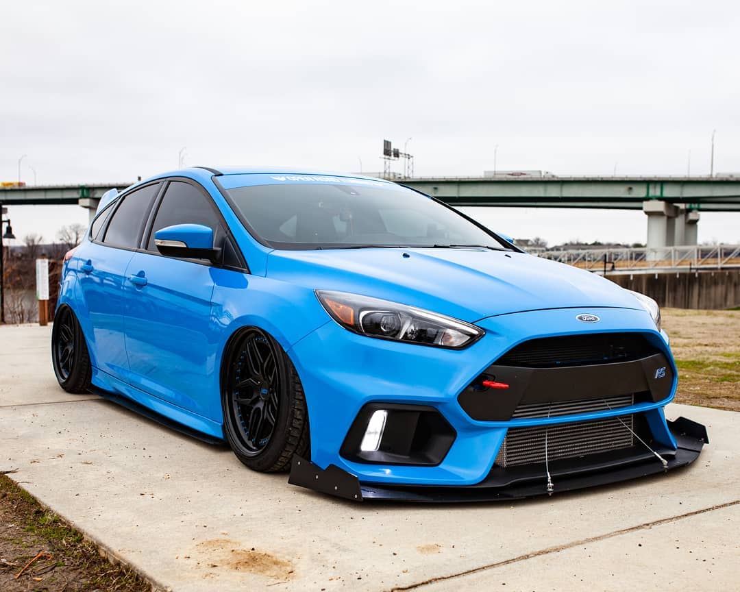 Front view of a slammed blue Focus RS with wide front splitter near a bridge