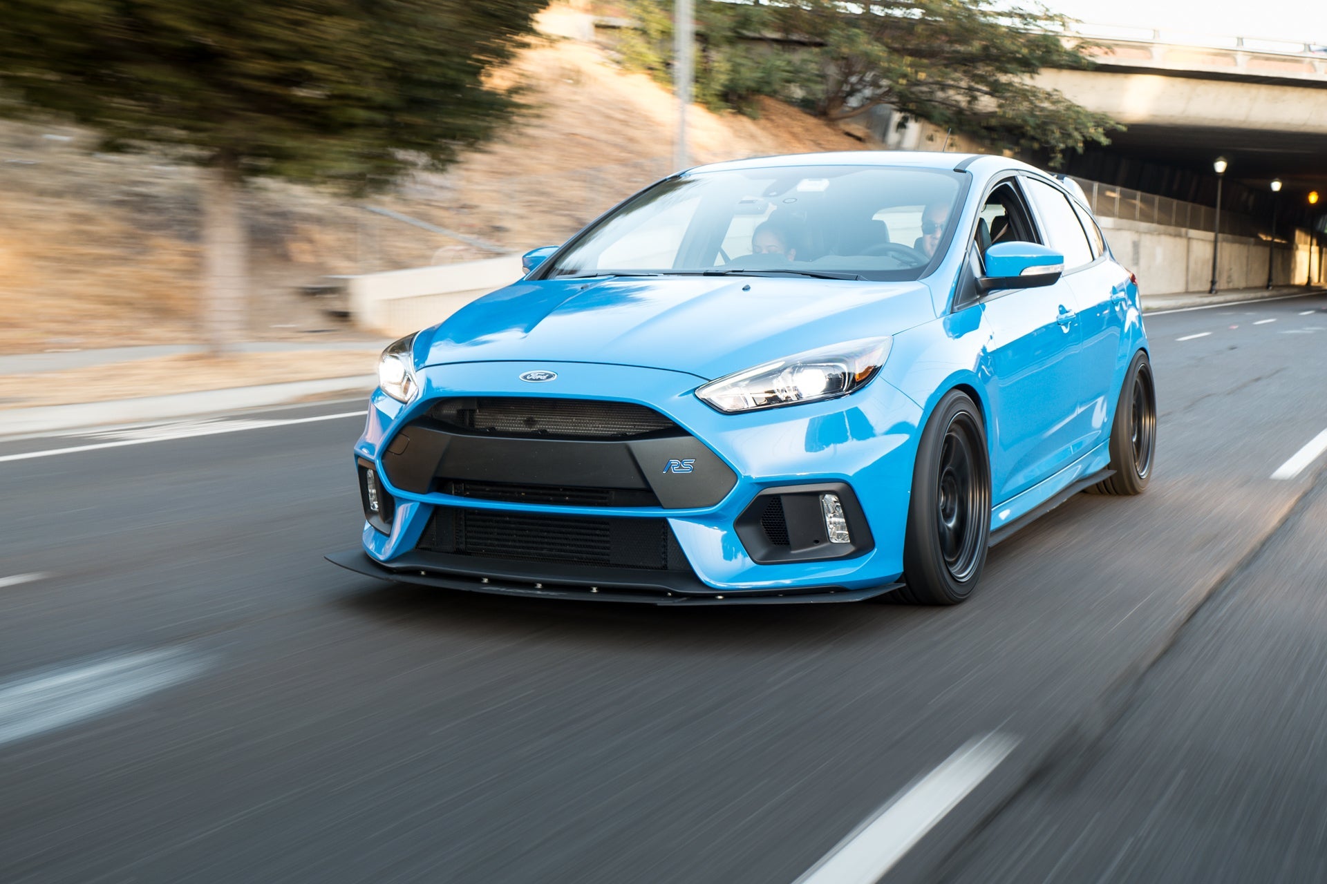 Blue Ford Focus RS with Epsilon+ front lip driving through a highway tunnel