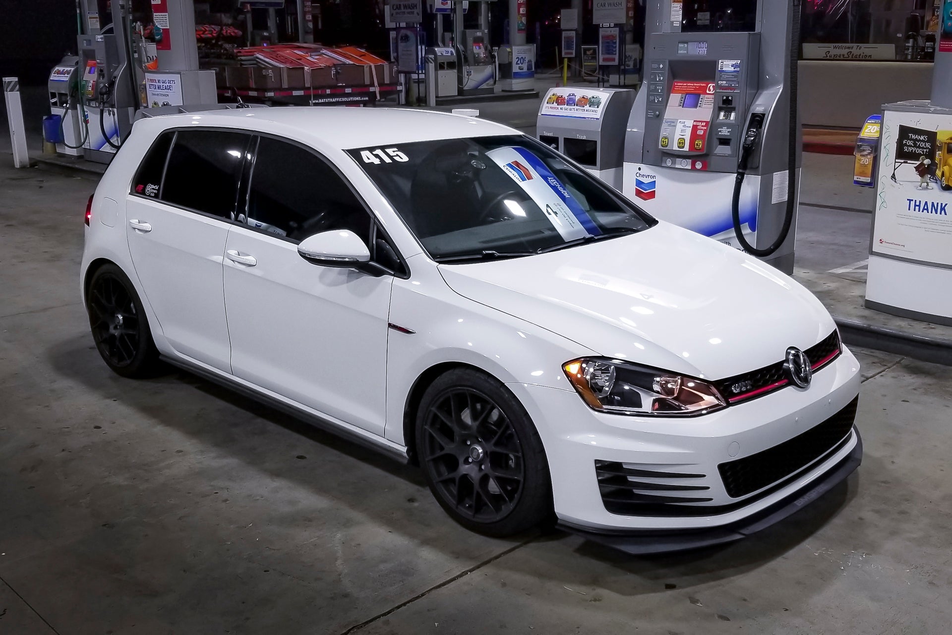 Front three-quarter view of a white Golf GTI with front lip at a gas station