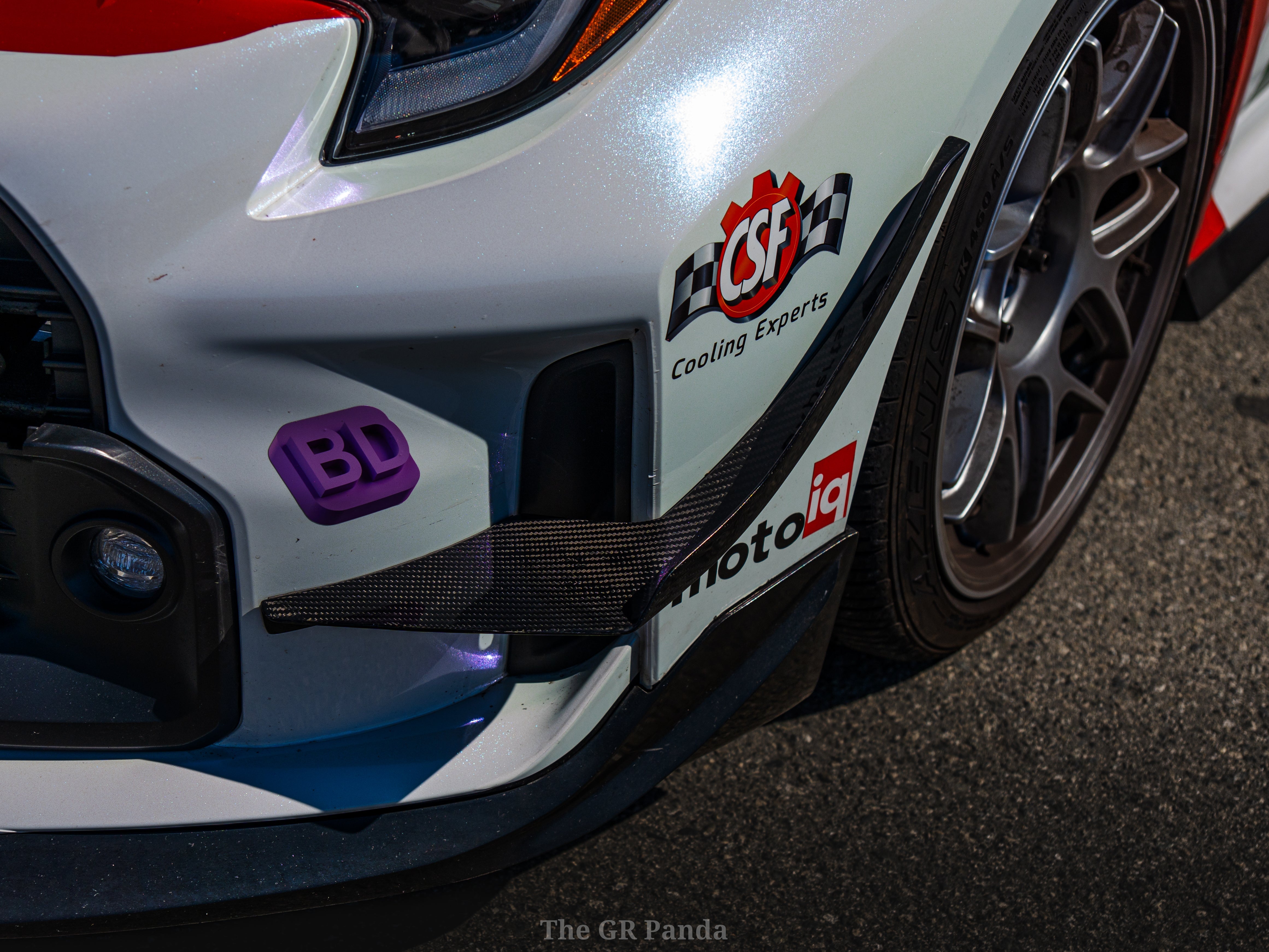 Close-up of a canard mounted on a white and blue GR Corolla rally car fender