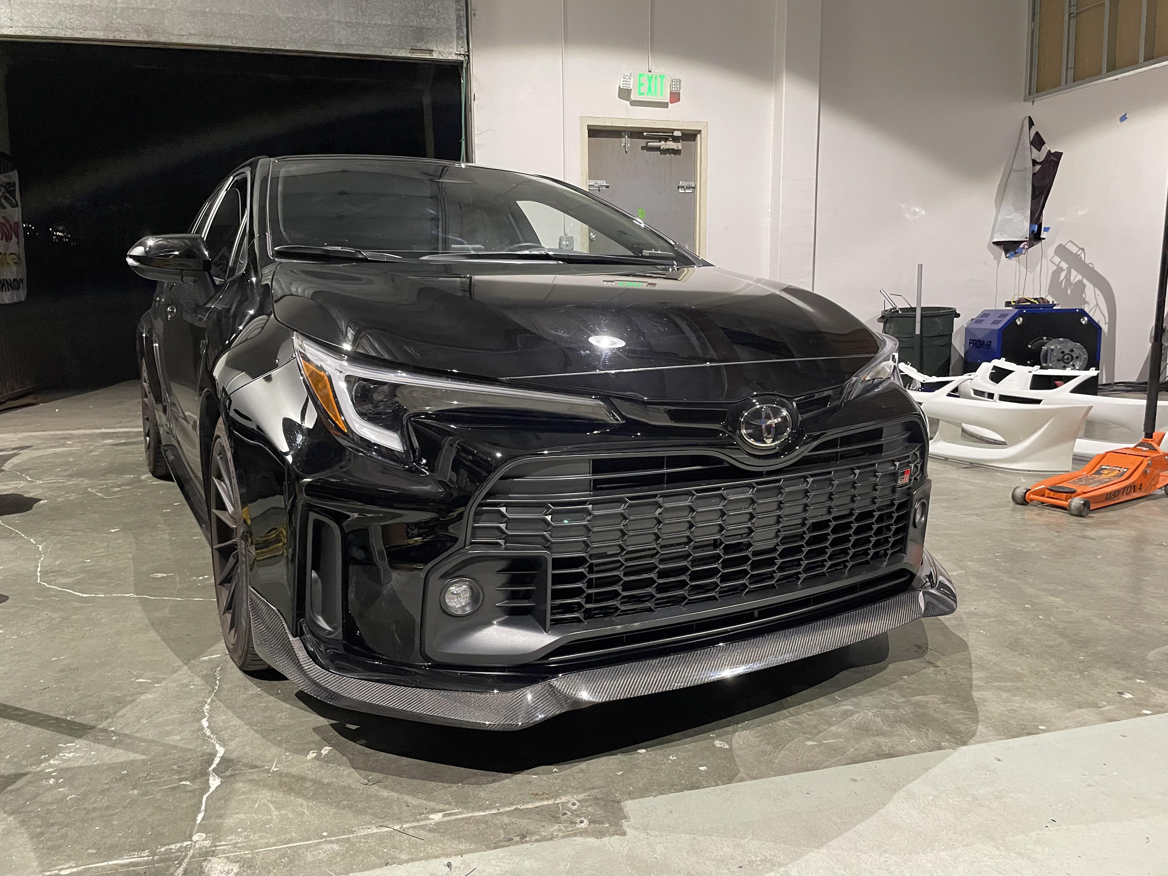 Close-up front fender view of a black GR Corolla with front lip and red brake calipers