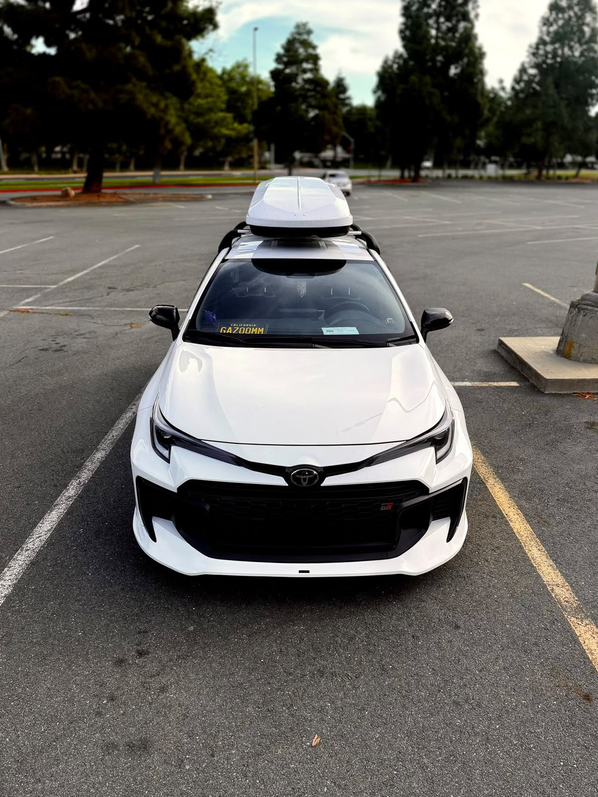Elevated front view of a white GR Corolla Kouki with front lip and roof box in a parking lot