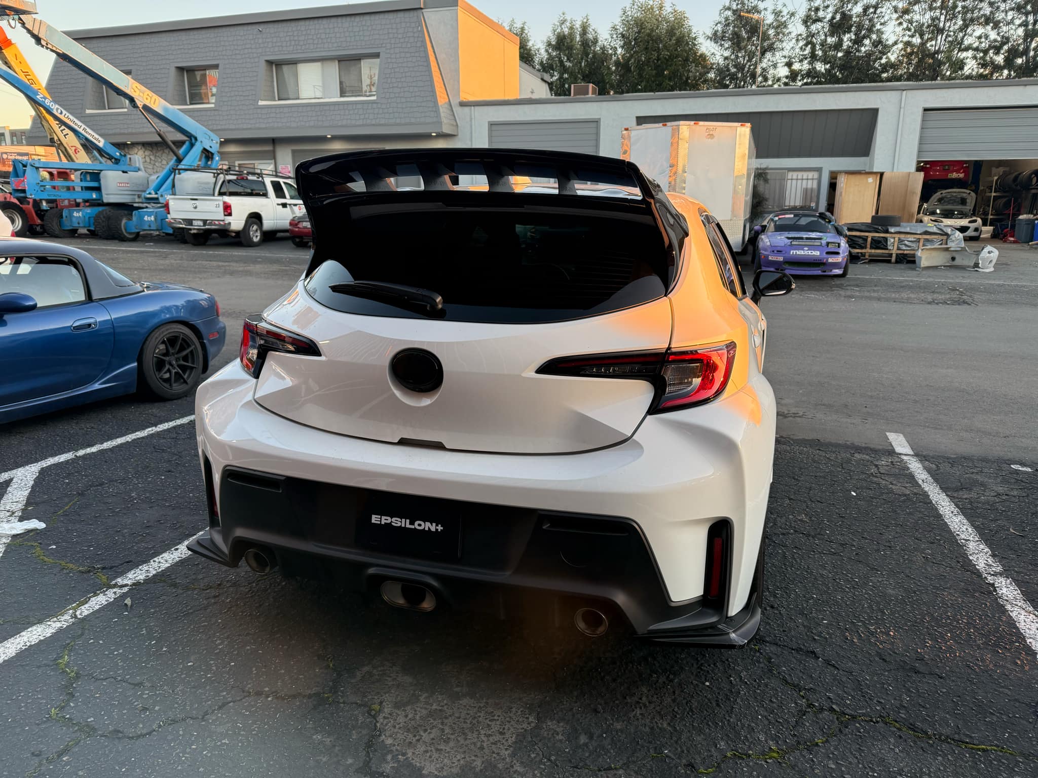 Rear view of a white GR Corolla with WRC Wing Strakes V2 near other cars