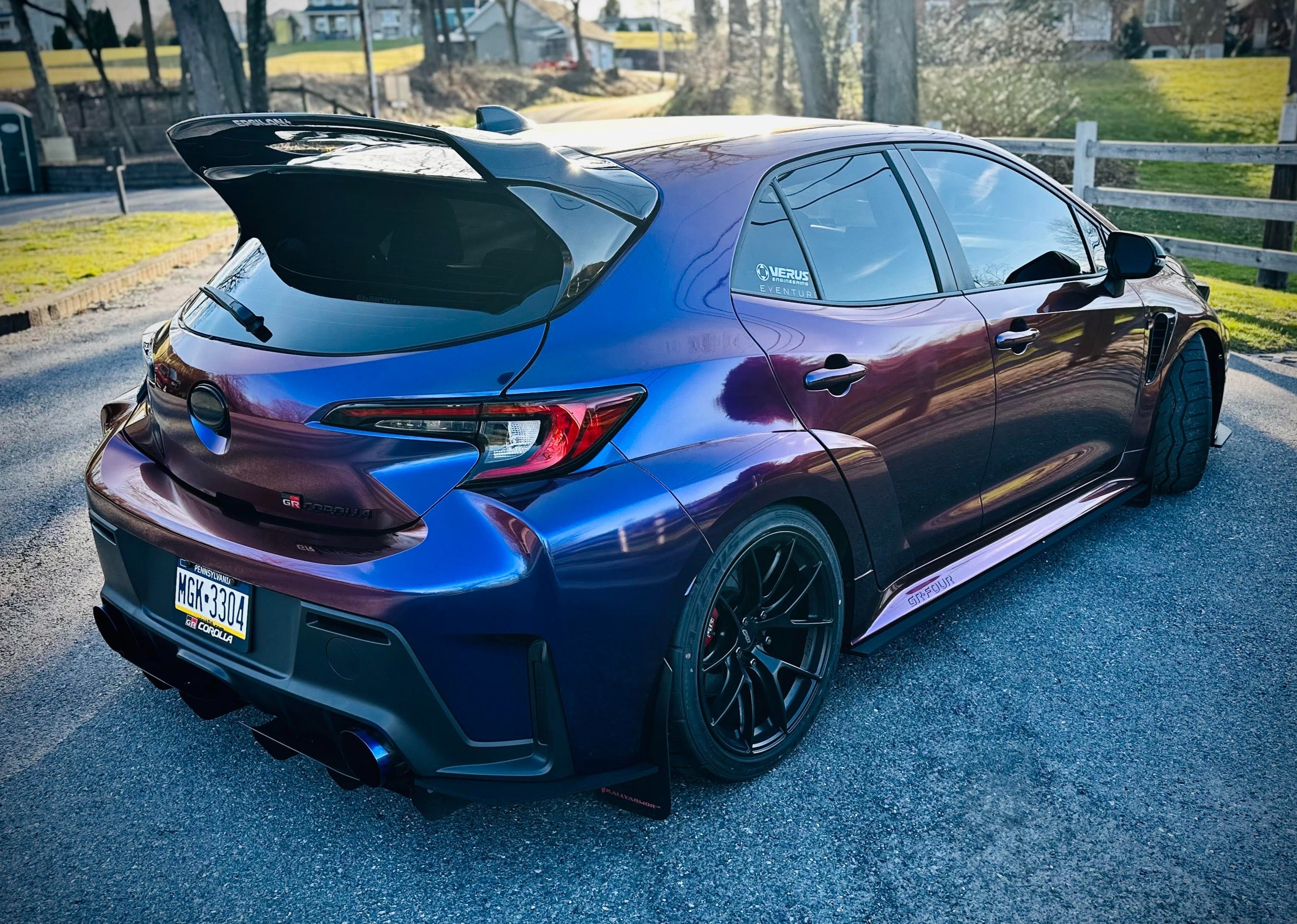 Rear three-quarter view of a purple color-shift GR Corolla with WRC Wing V3 on a country road