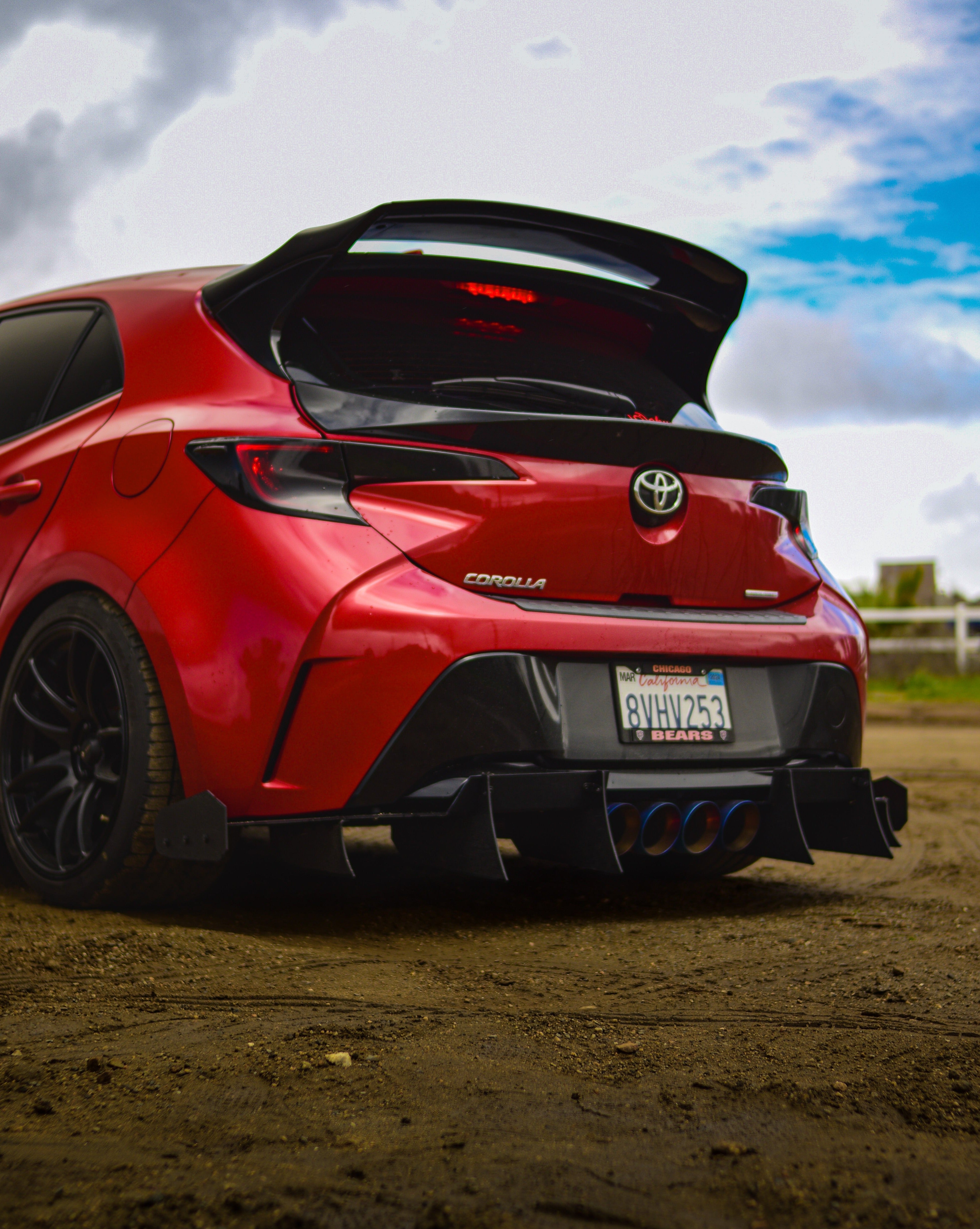 Rear three-quarter view of a red GR Corolla with WRC Wing V3 on a dirt road