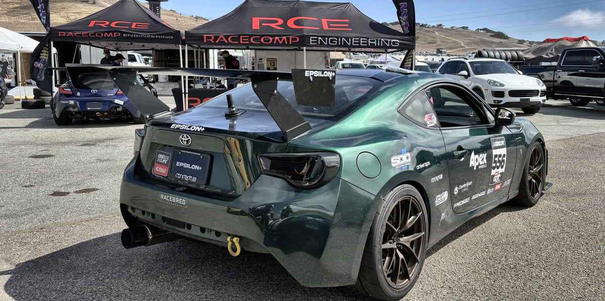 Green Toyota GT86 race car with the Epsilon+ TC Wing, rear three-quarter view in the Laguna Seca paddock