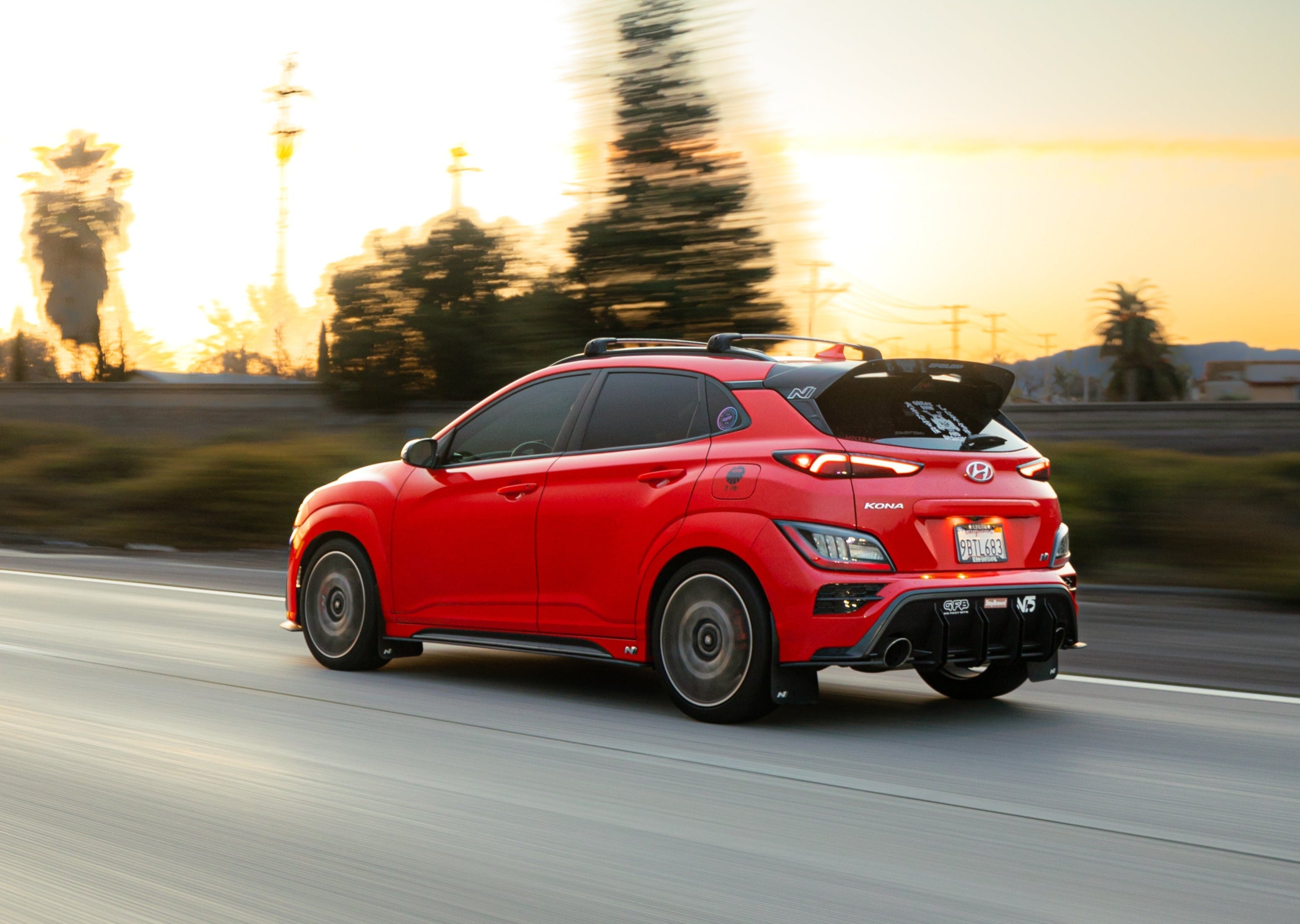 Side profile of a red Hyundai Kona N with spoiler extension driving at sunset