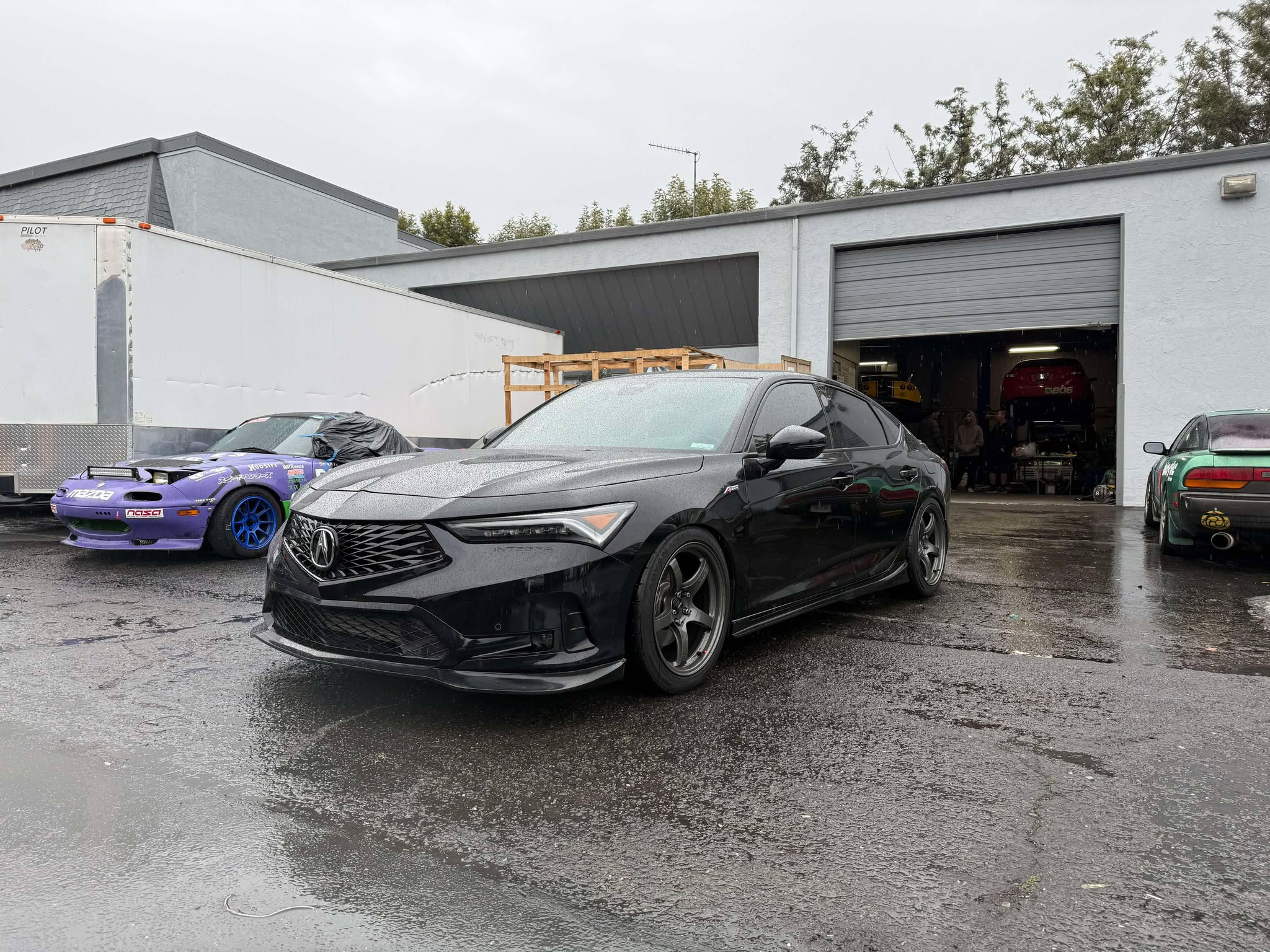 Front three-quarter view of a black Acura Integra with front lip at a shop