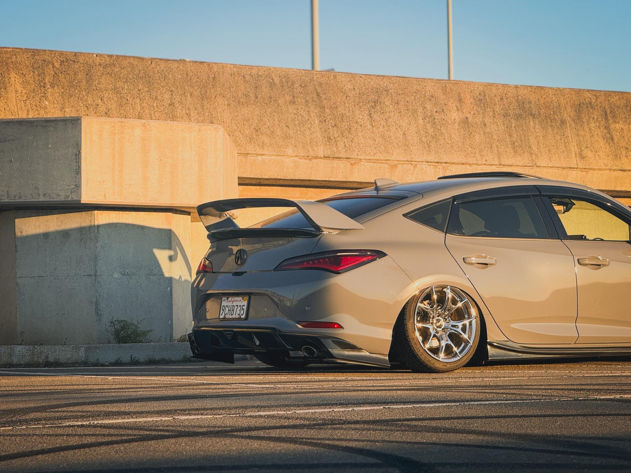 Low rear view of a gray Acura Integra with the Sport Wing beside a concrete wall