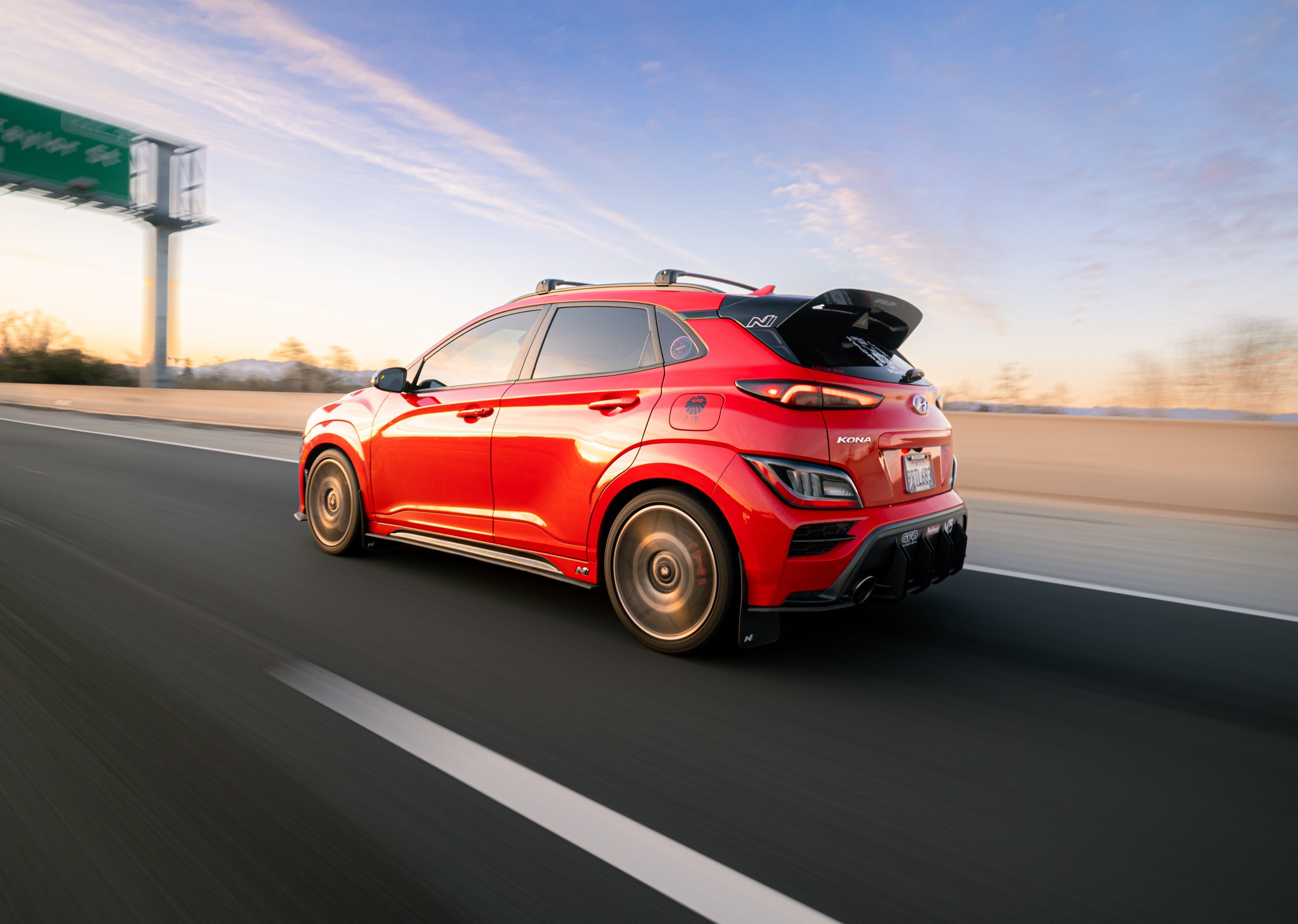 Rear three-quarter view of a red Kona N with spoiler extension on a highway