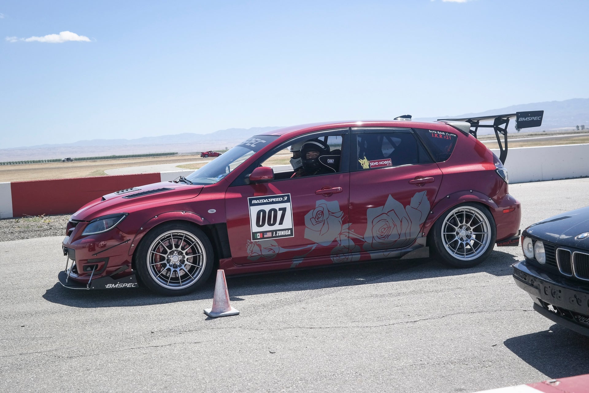 Red Mazdaspeed3 Gen1 motorsport car with GT wing on a track, race number 007