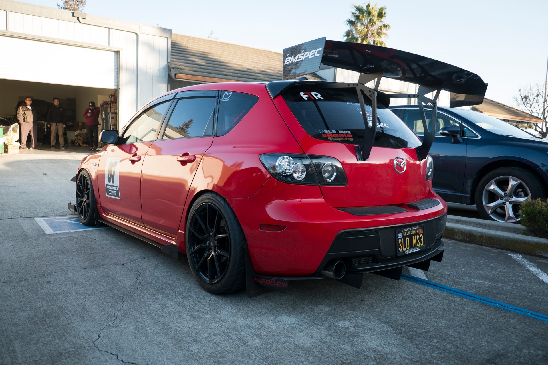 Rear three-quarter view of a red Mazdaspeed3 Gen1 with GT wing in a parking lot