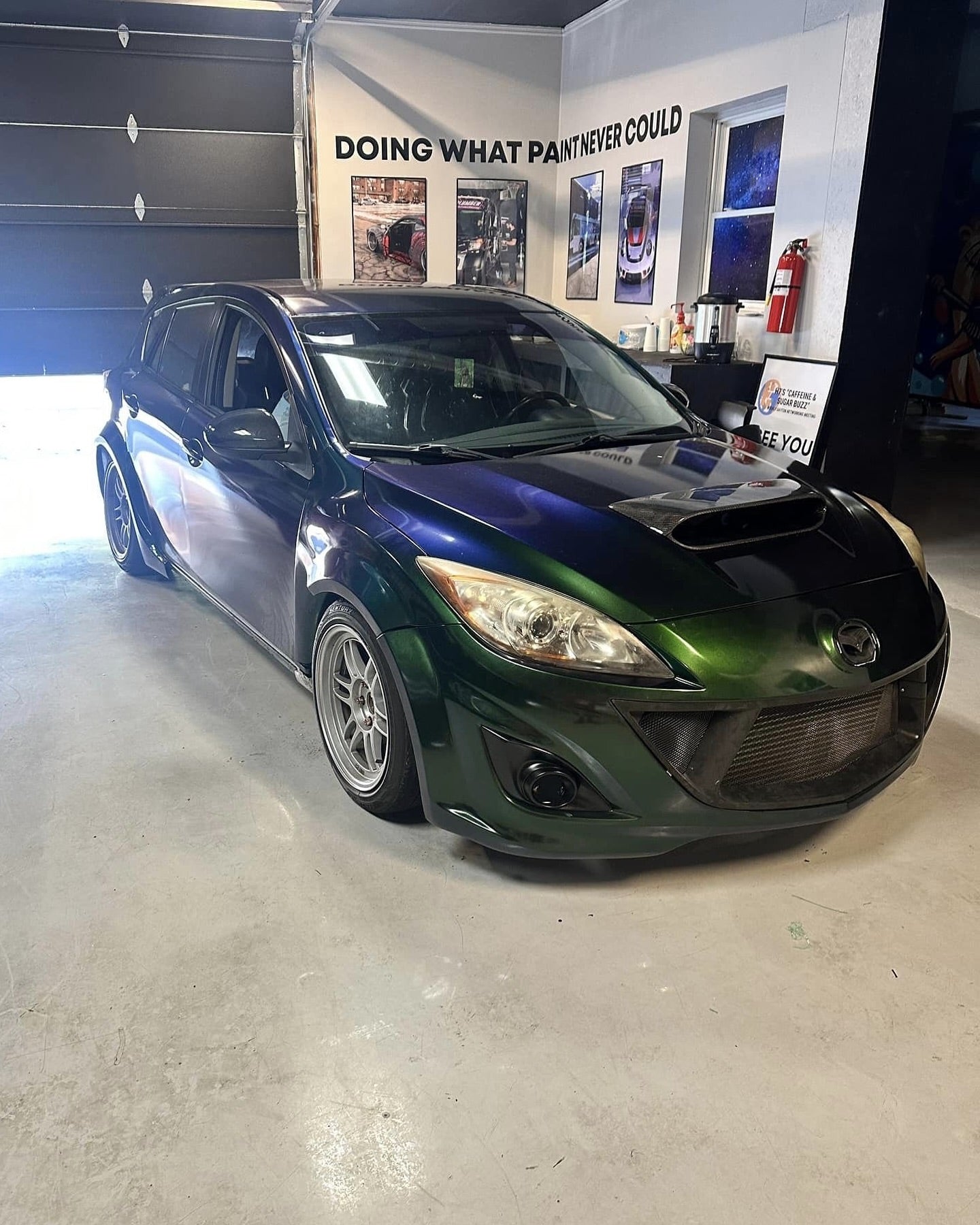 Dark Mazdaspeed3 BL with widebody fender flares inside a workshop
