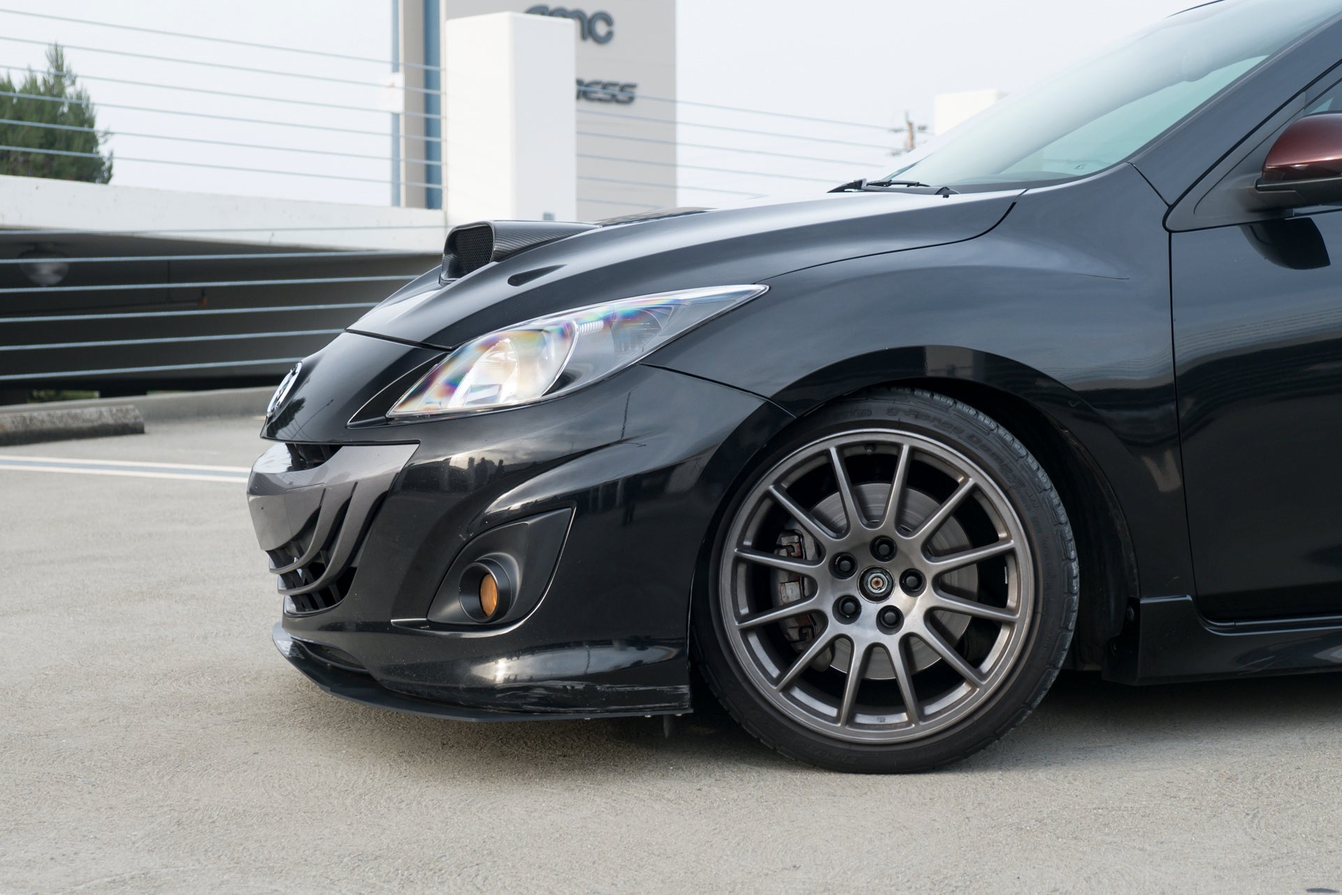 Front three-quarter view of a black Mazdaspeed3 Gen2 with front lip, showing wheel fitment