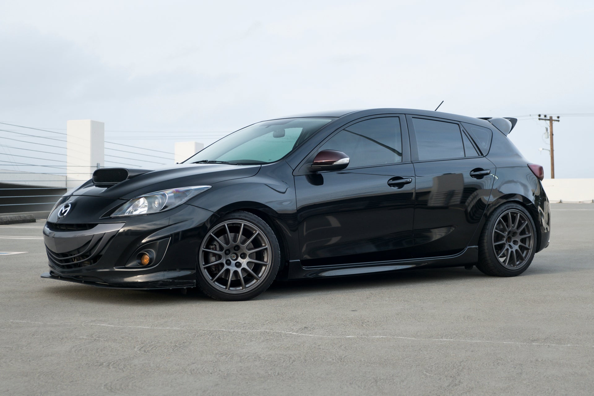 Side profile of a black Mazdaspeed3 Gen2 with front lip, parked in a lot