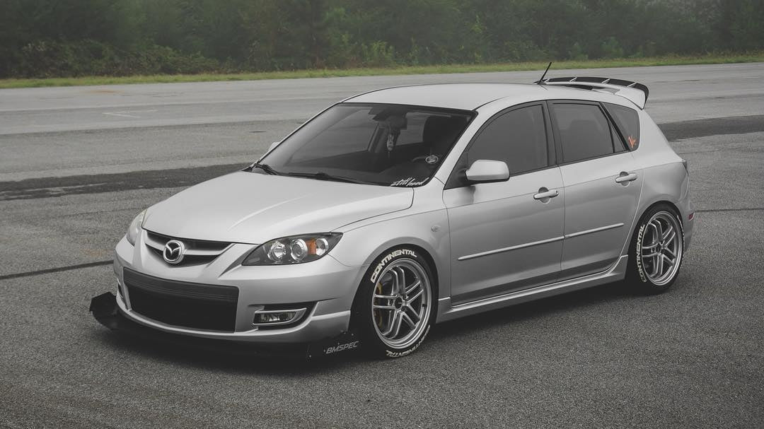 Silver Mazdaspeed3 Gen1 with spoiler extension parked on a track, studio-style edit