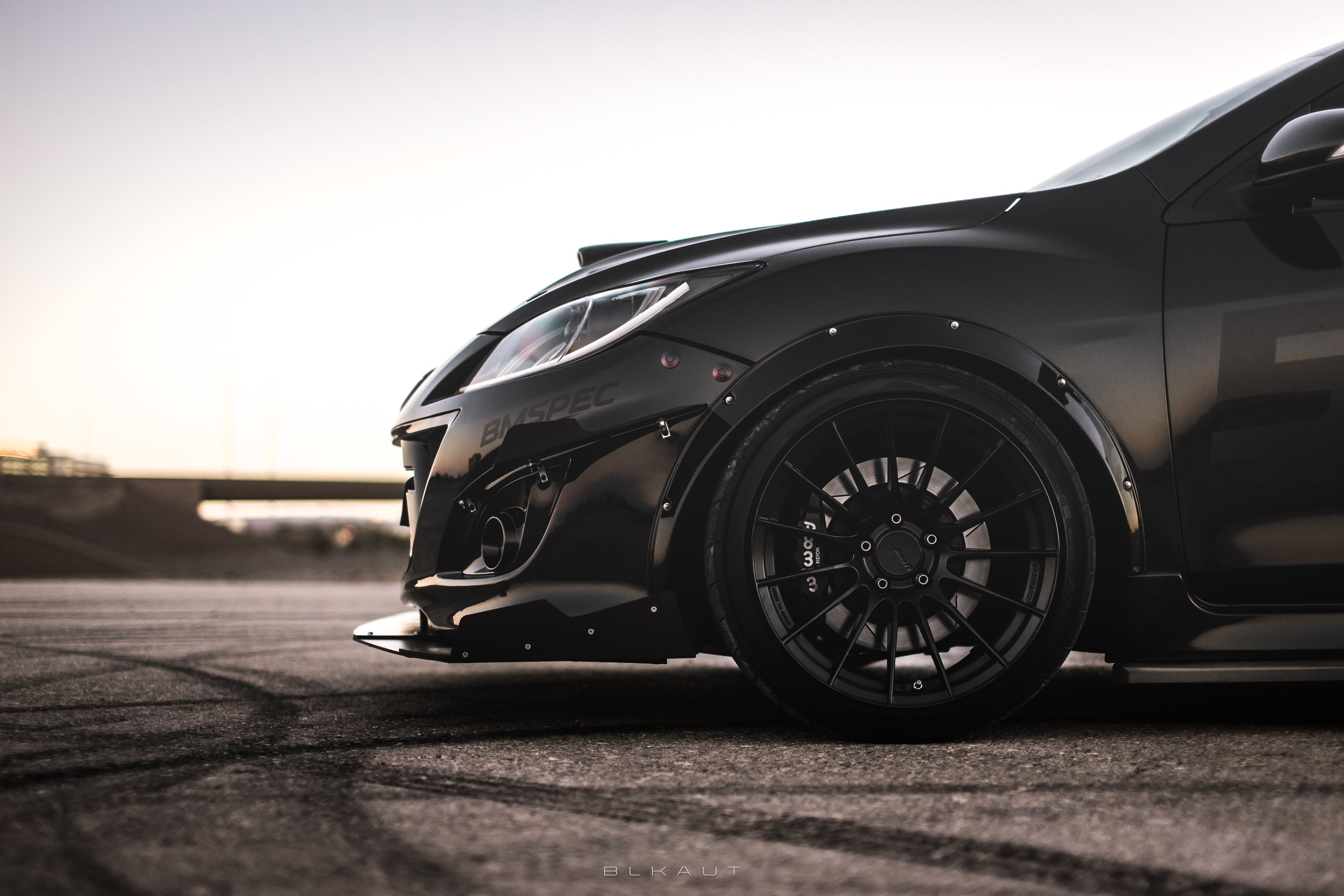 Front three-quarter close-up of a black Mazdaspeed3 Gen2 with front splitter at sunset