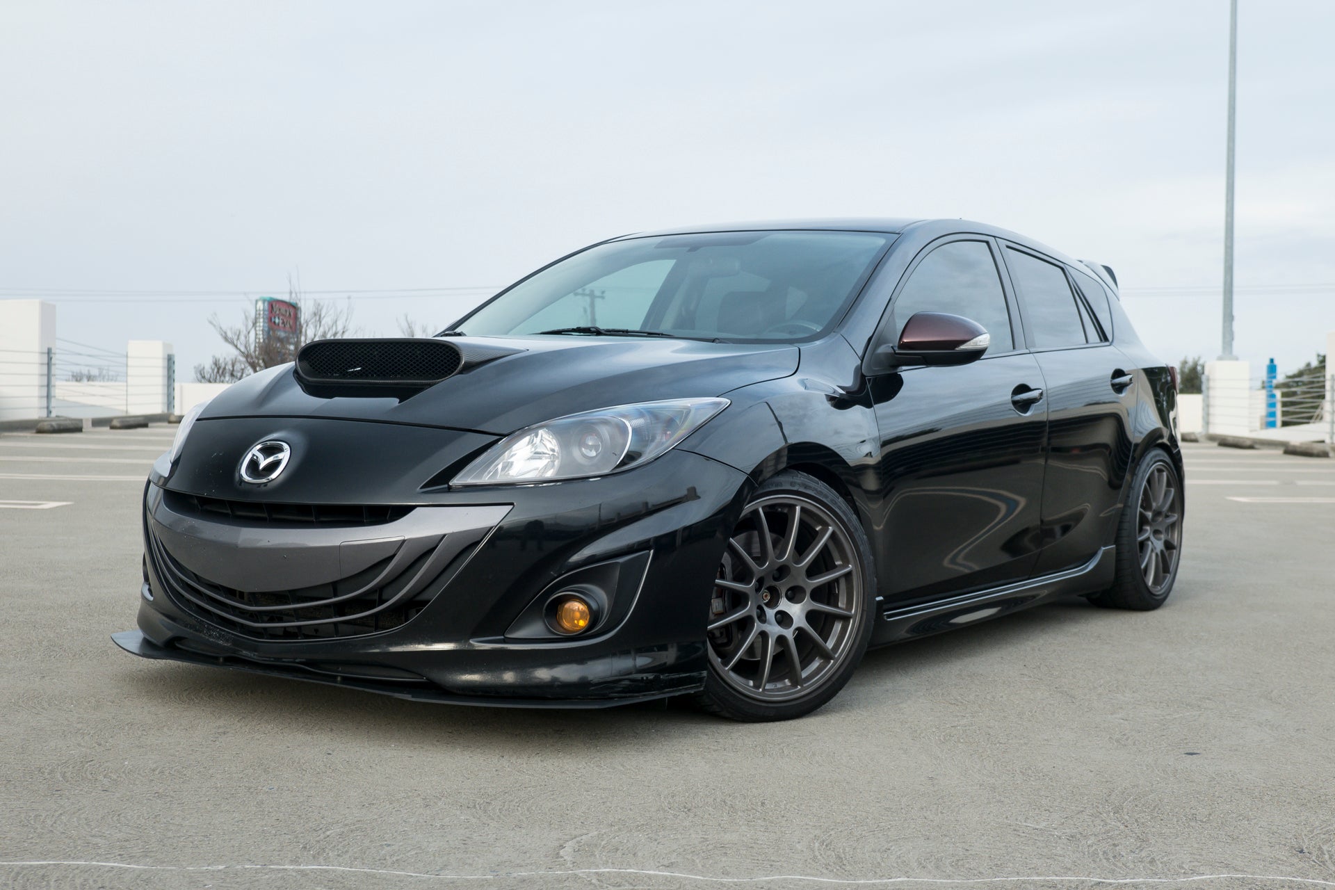 Front three-quarter view of a black Mazdaspeed3 Gen2 hatchback with Epsilon+ front lip installed