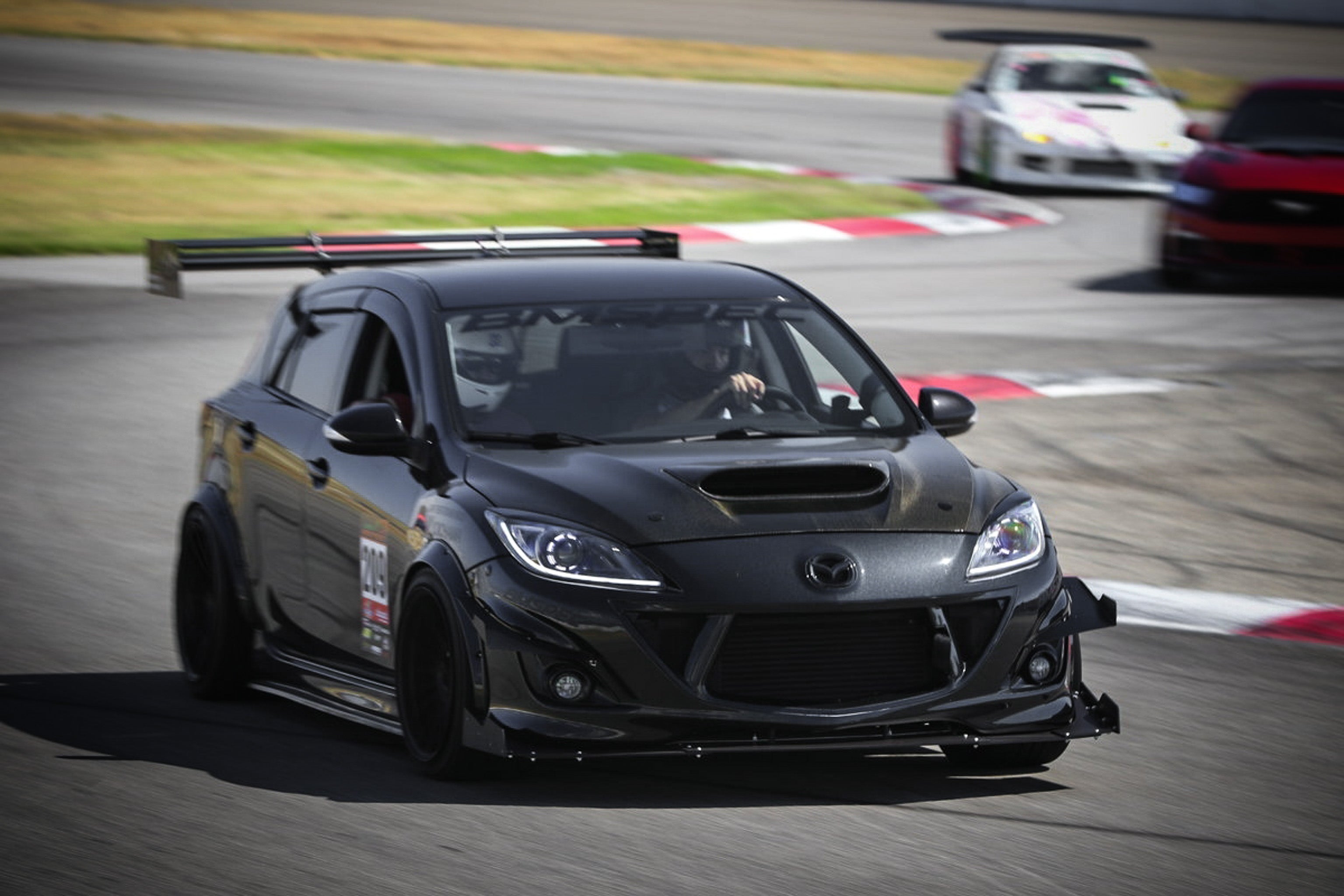 Black Mazdaspeed3 Gen2 with front splitter driving on a race track straightaway