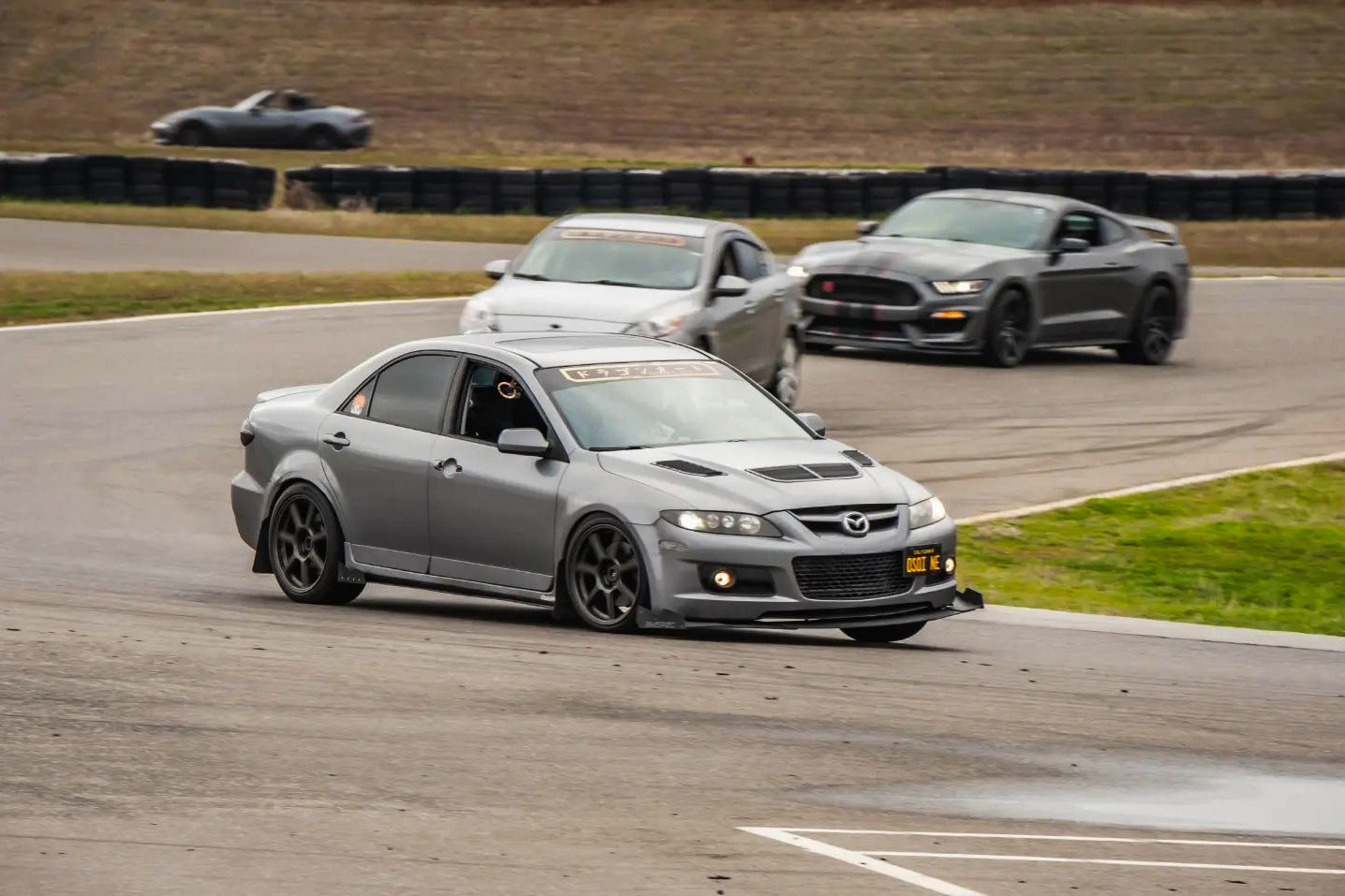 Gray Mazdaspeed6 with front splitter cornering on a track alongside other cars
