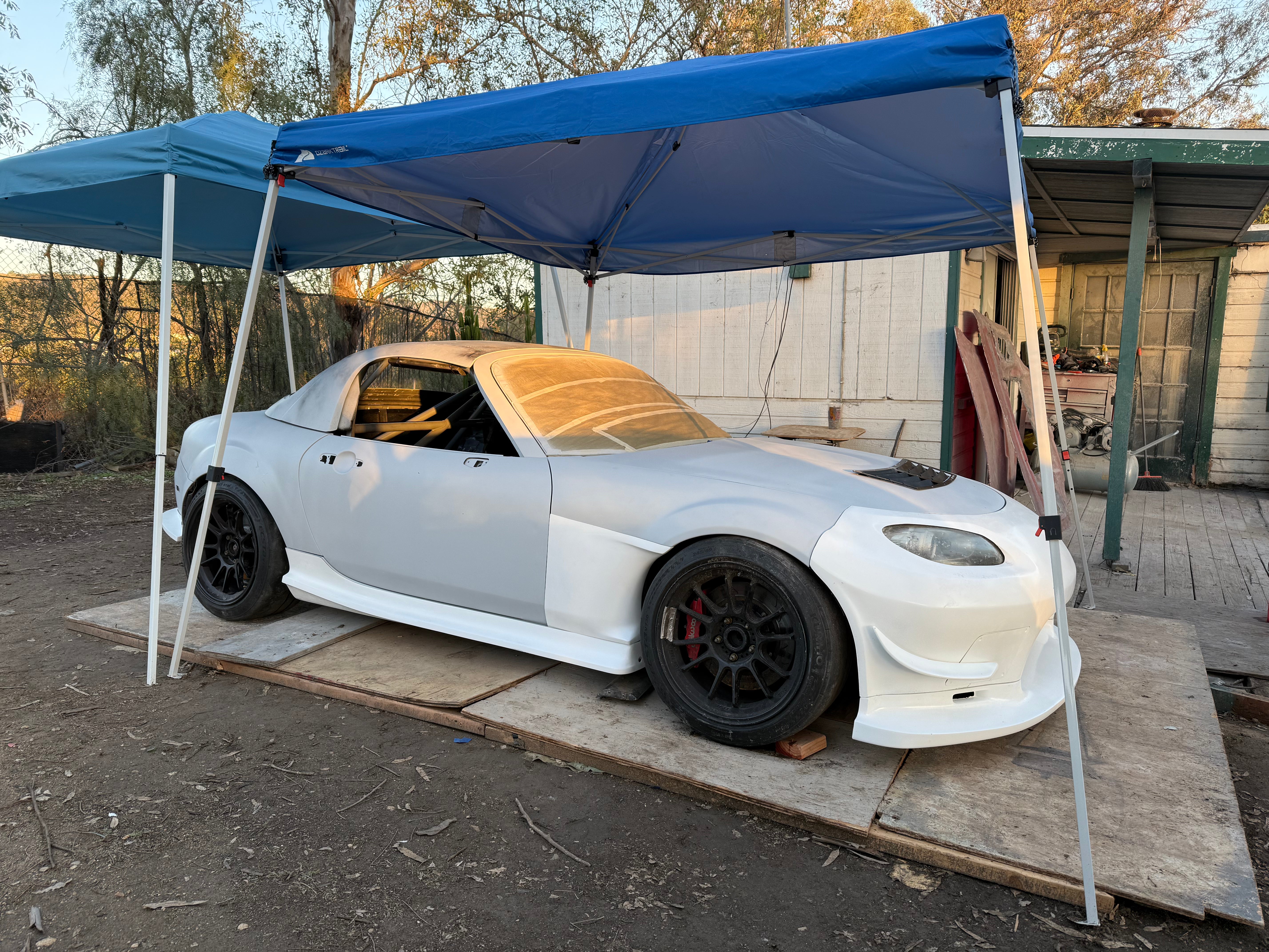 White Mazda MX-5 Miata NC with the unpainted Epsilon+ aero kit fitted under a canopy