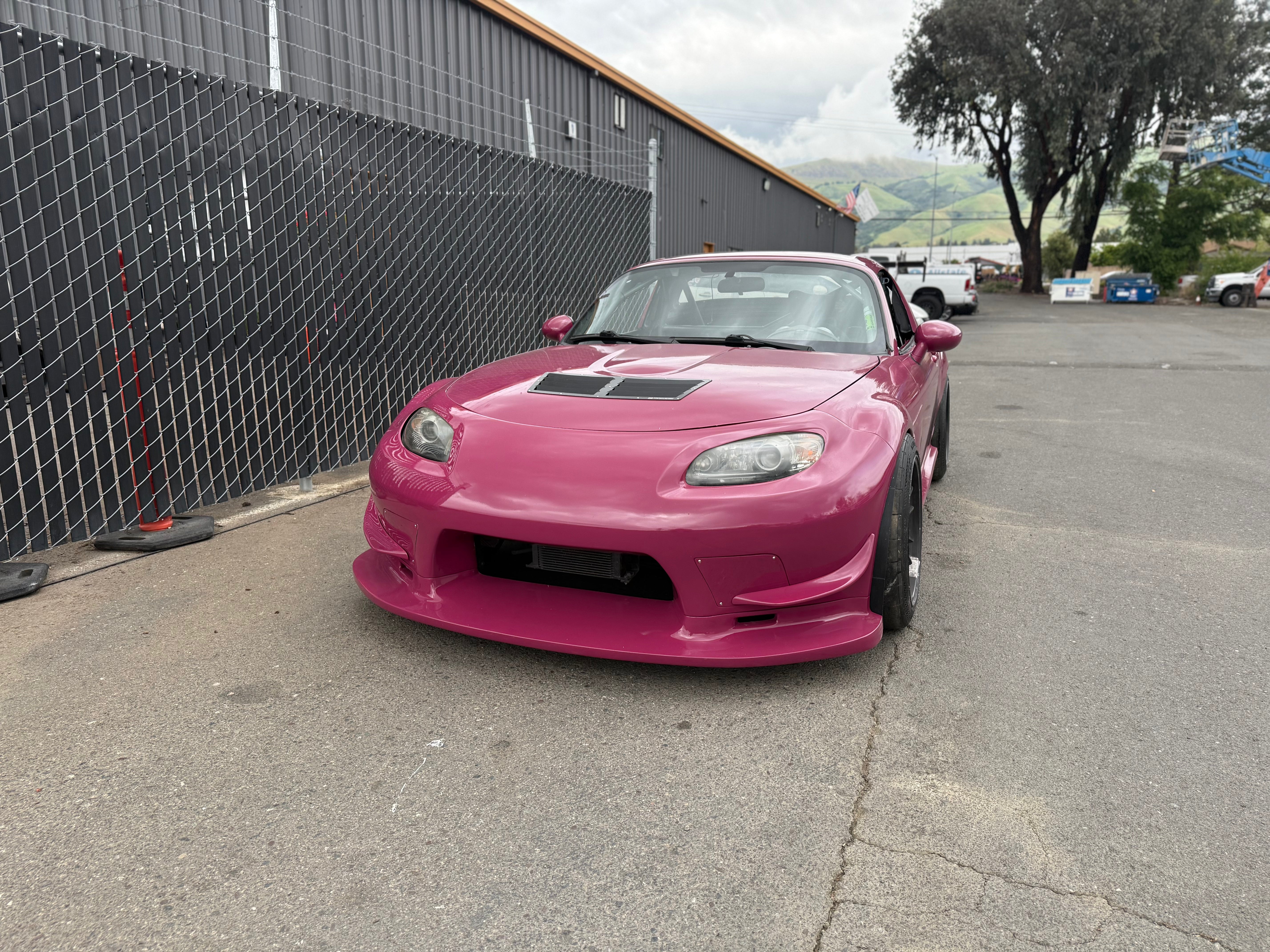 Elevated front three-quarter view of a pink Mazda MX-5 Miata NC with canards