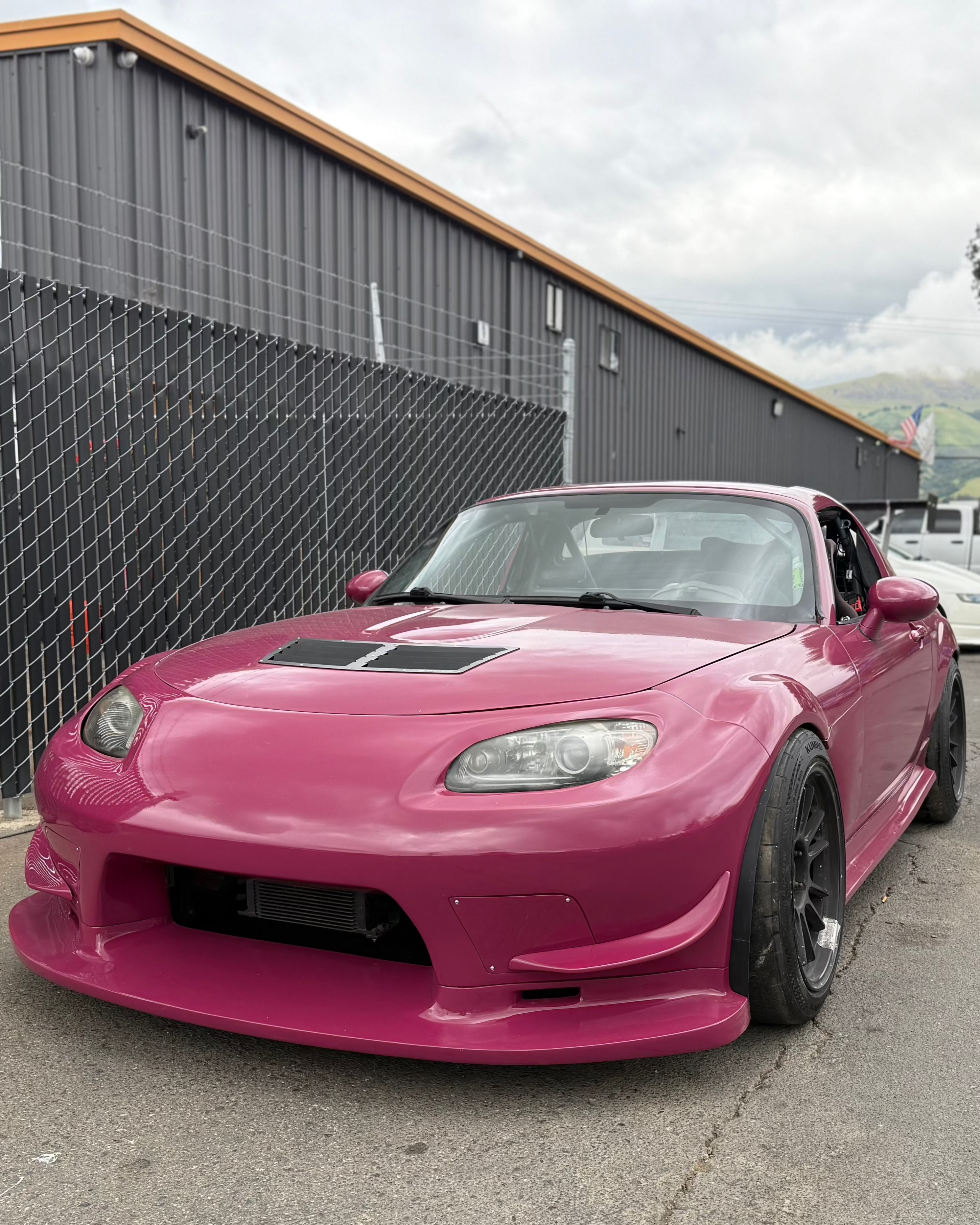 Front three-quarter view of a pink Miata NC with the Epsilon+ front bumper and vented hood