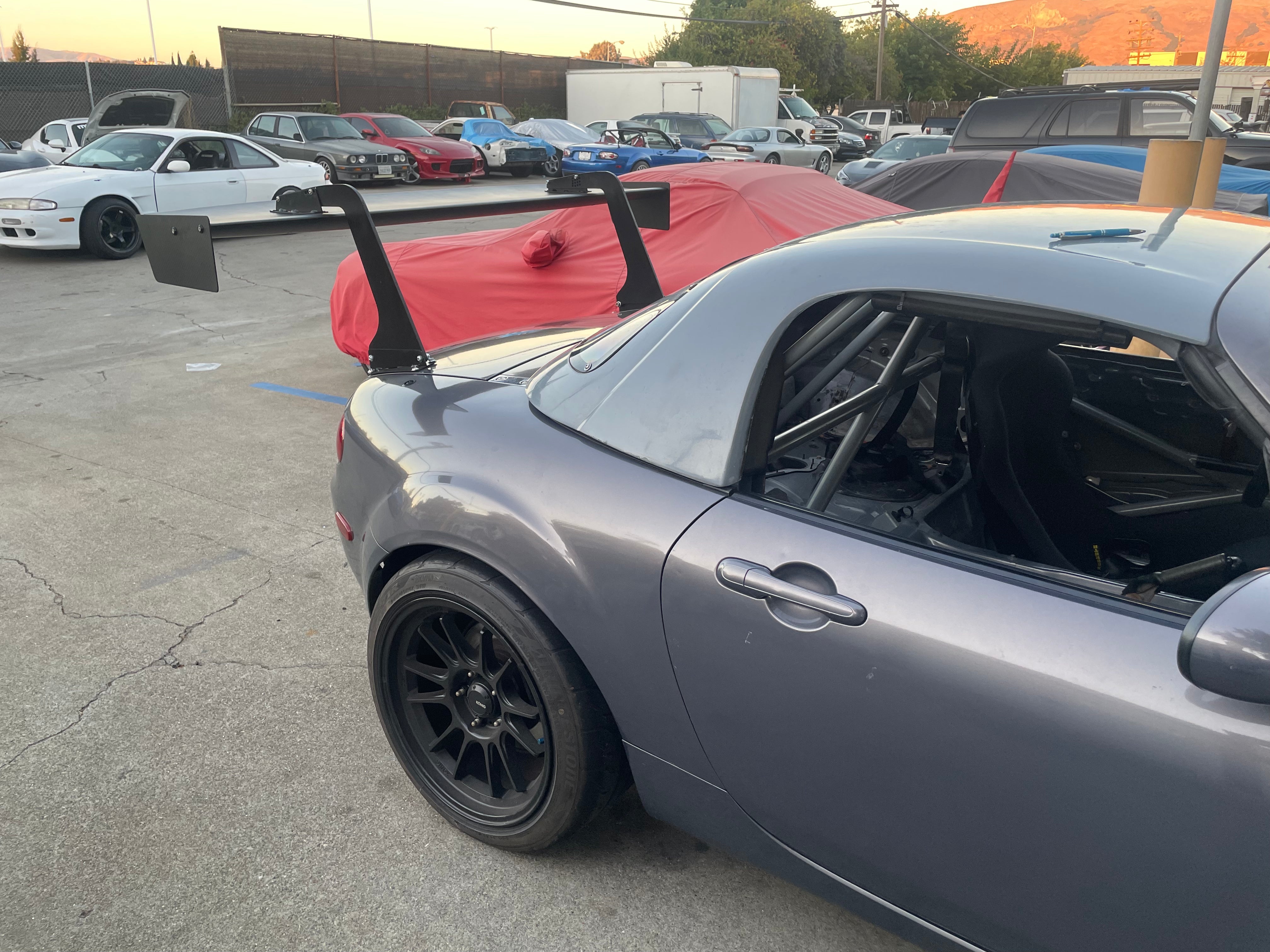 Side profile of a gray Mazda MX-5 Miata NC with roll bar and GT wing