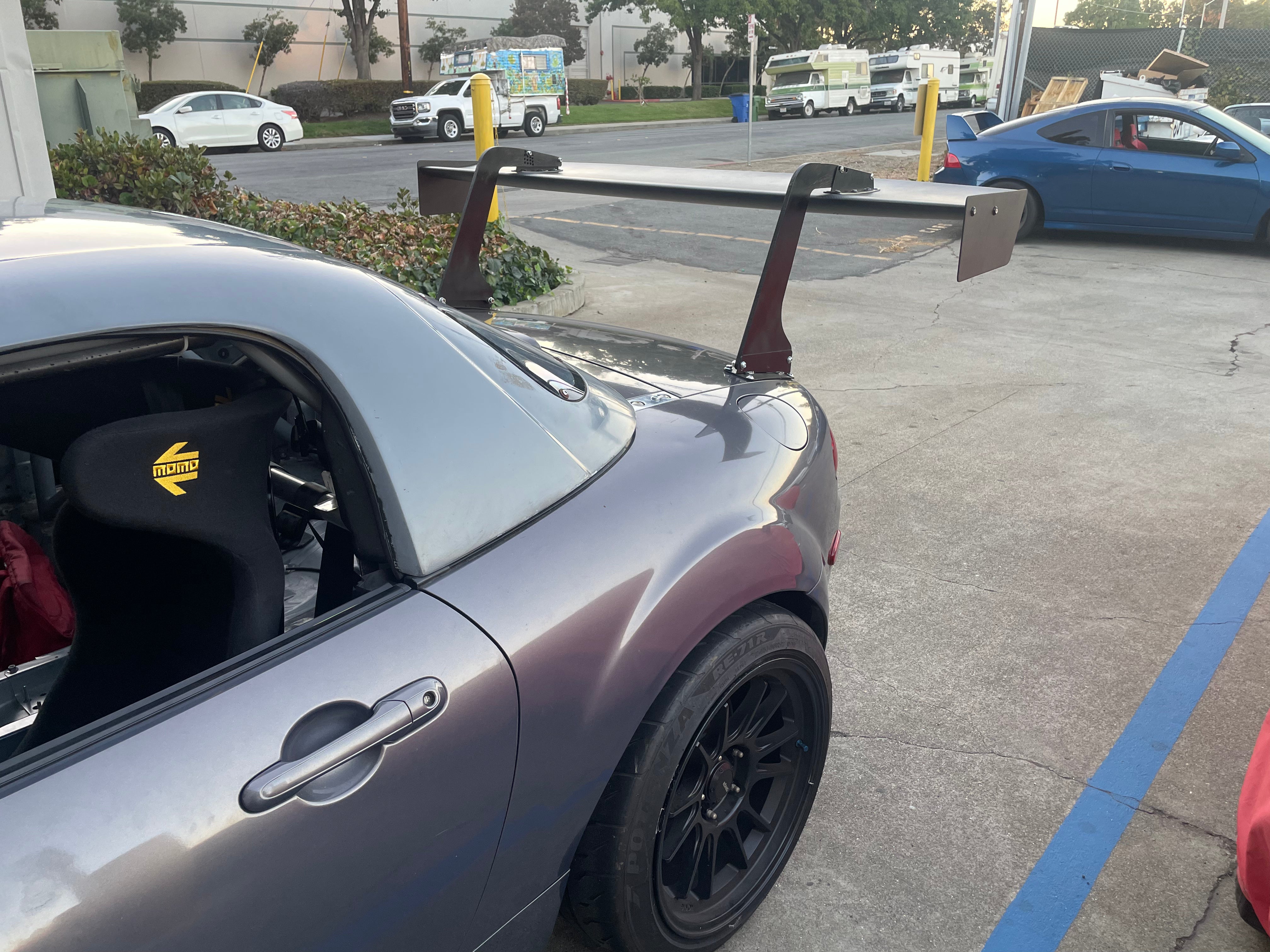 Side-rear view of a gray Mazda MX-5 Miata NC showing the GT wing uprights
