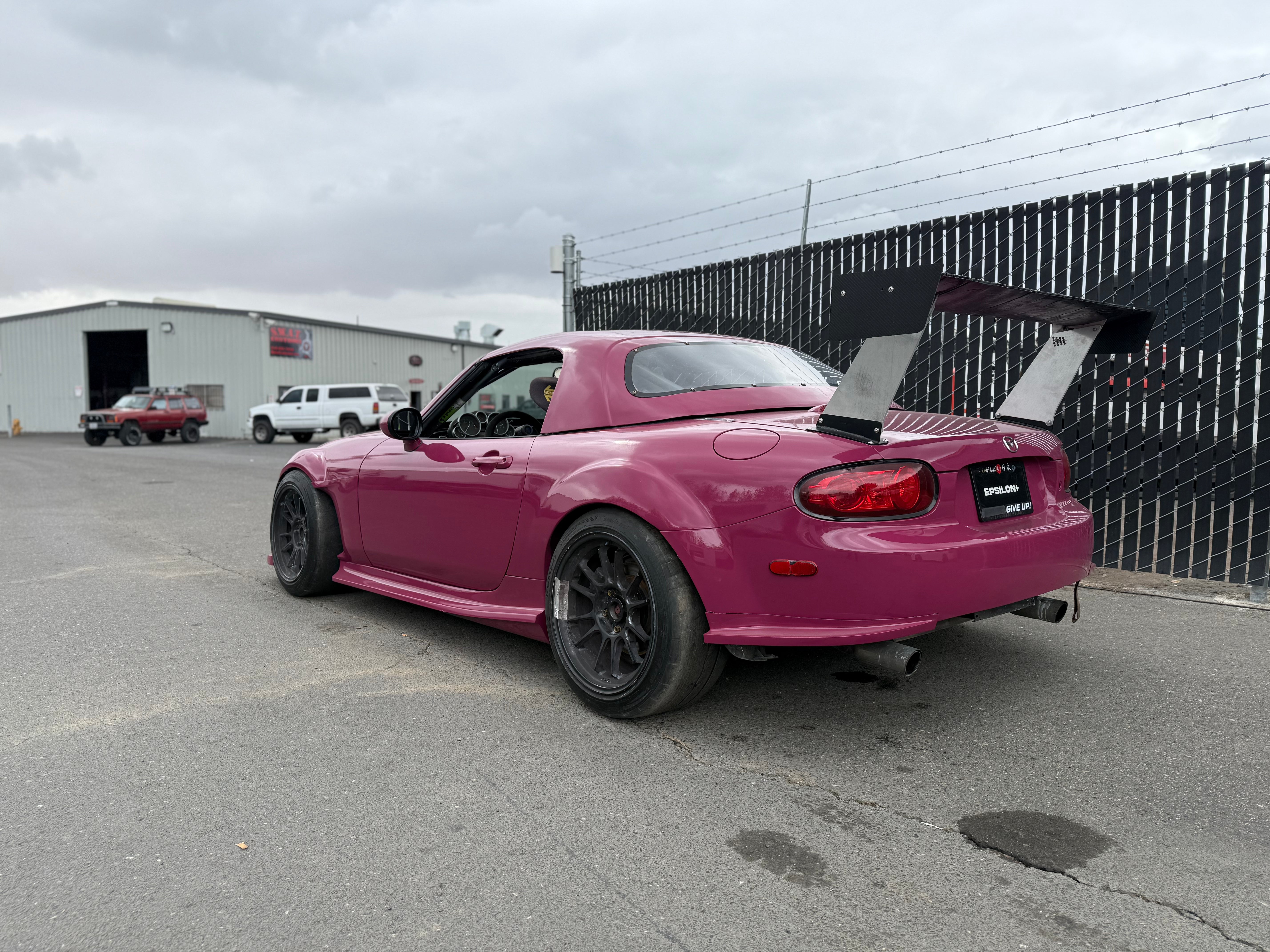 Rear three-quarter view of a pink Mazda MX-5 Miata NC with side skirts and rear wing
