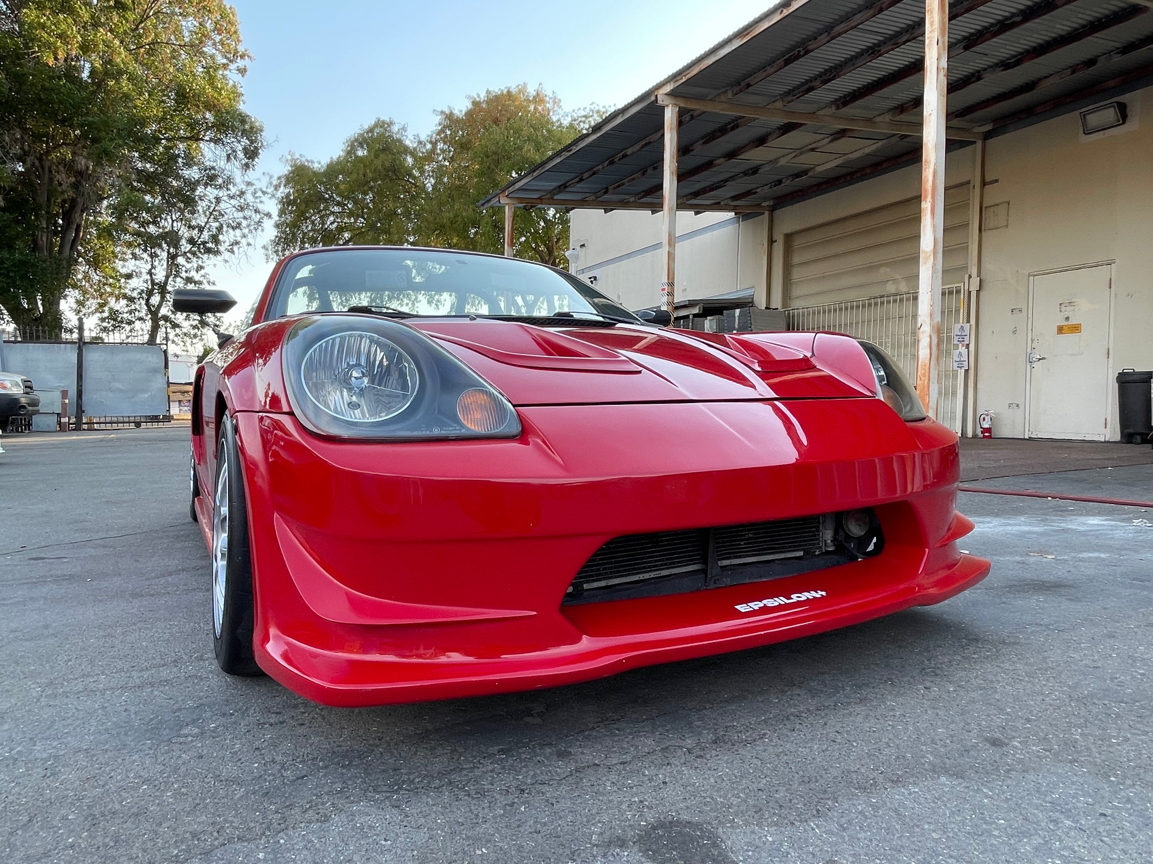 Low front three-quarter view of a red MR2 Spyder showing the front bumper and splitter