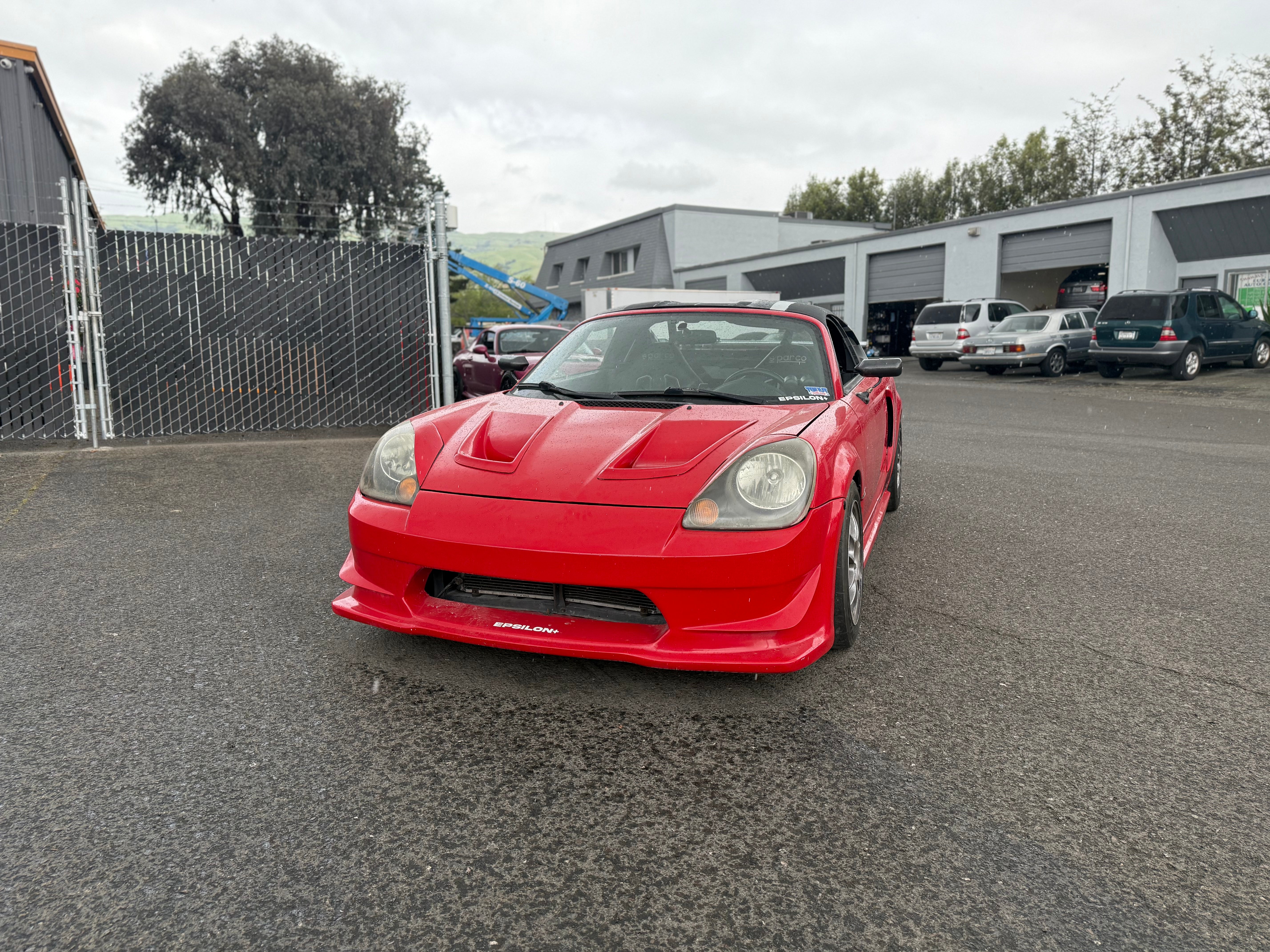Front three-quarter view of a red MR2 Spyder in an industrial car park