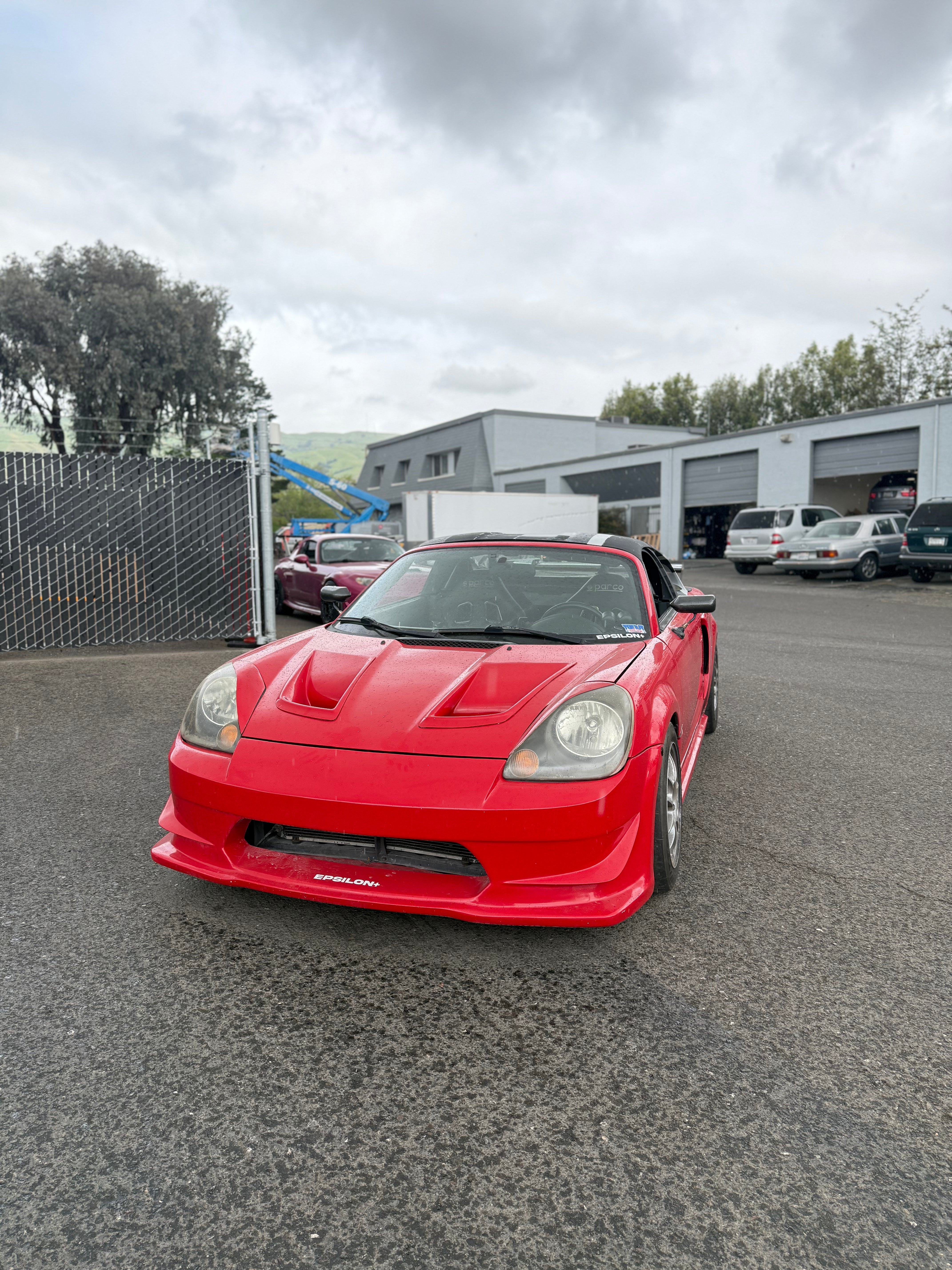 Front three-quarter view of a red Toyota MR2 Spyder outside an industrial unit