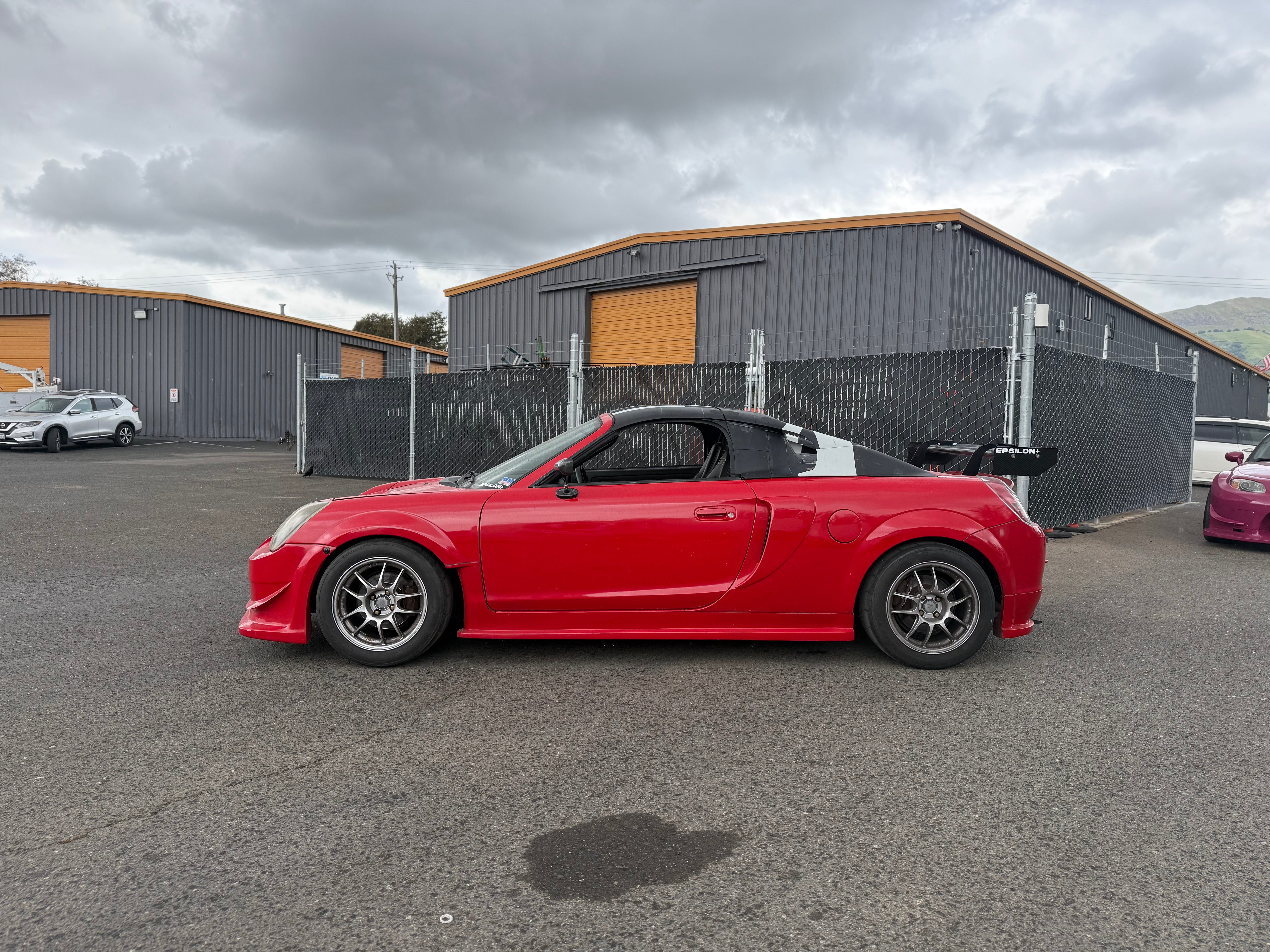 Side profile of a red MR2 Spyder parked outside a warehouse unit