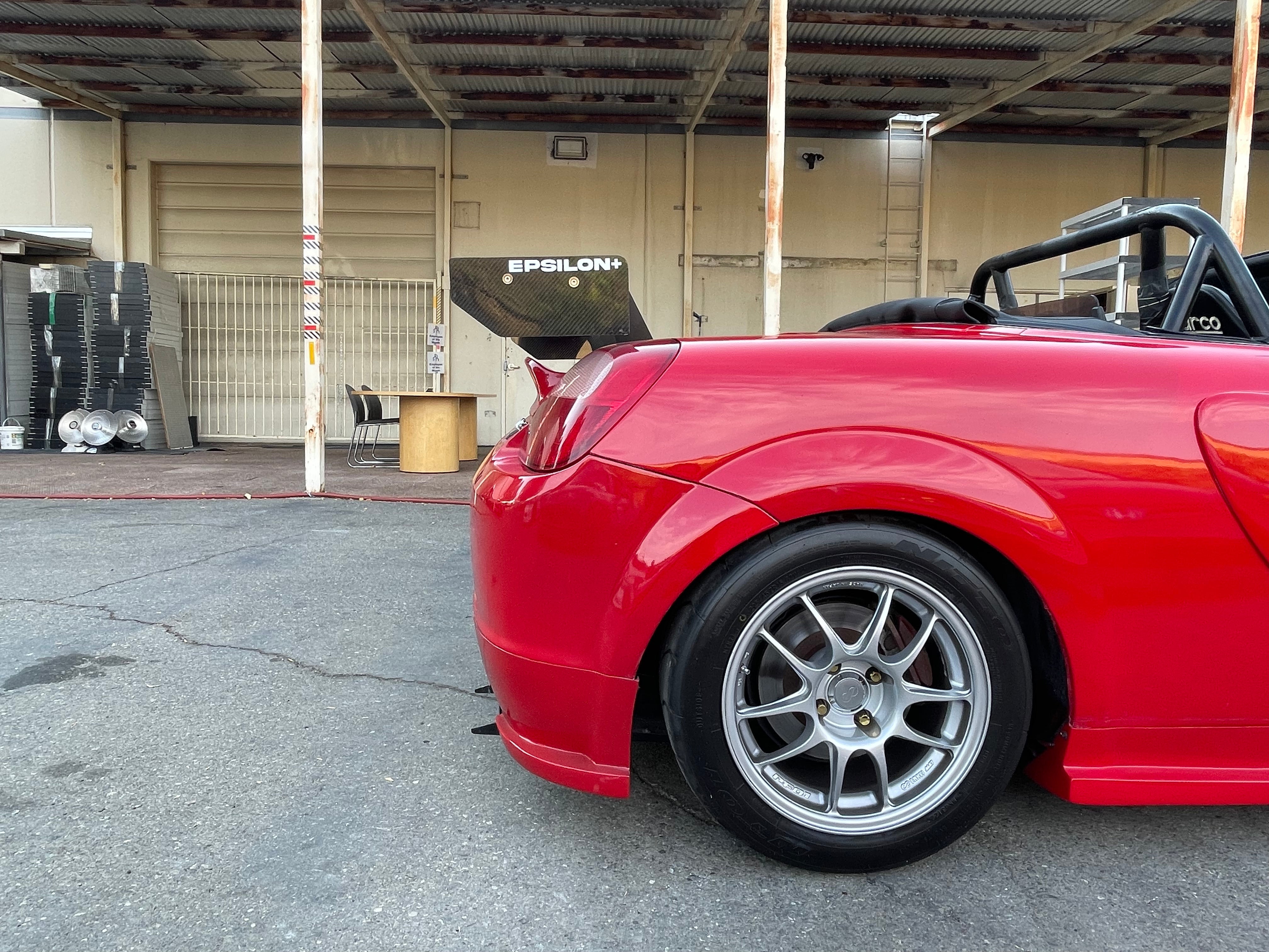 Side-rear view of a red MR2 Spyder showing the rear wing and side skirt profile