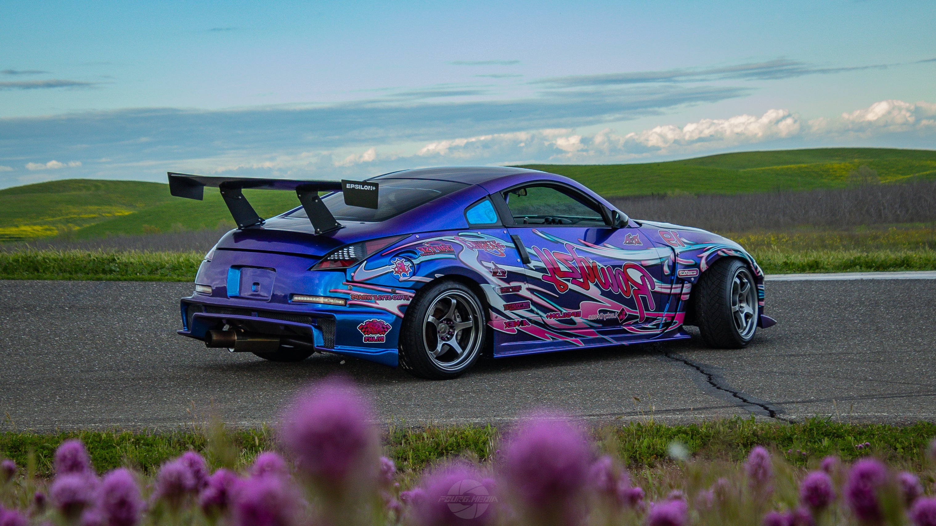 Rear three-quarter view of a purple liveried Nissan 350Z with GT wing near wildflowers