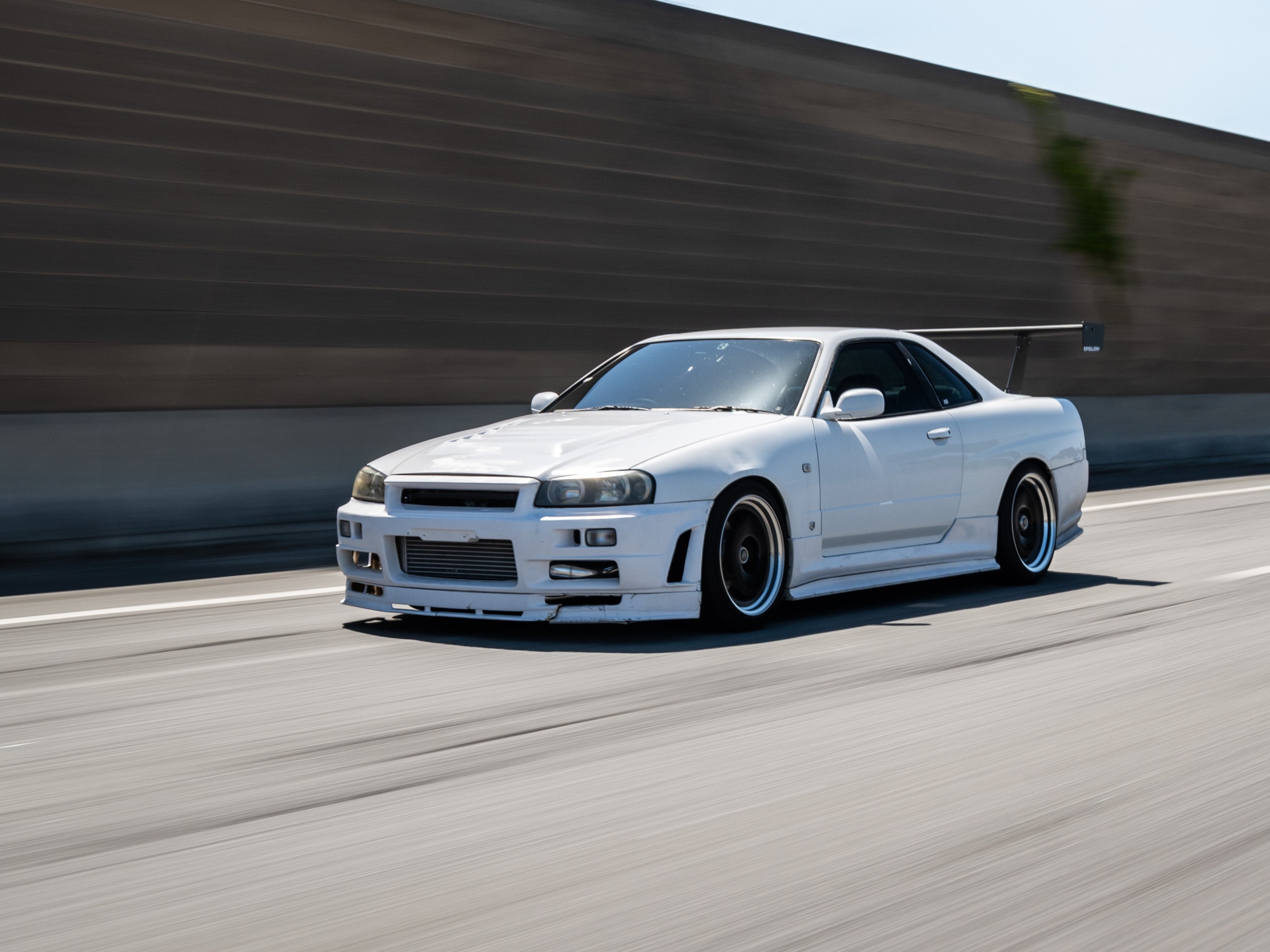 White Nissan Skyline R34 with Epsilon+ GT wing, front three-quarter rolling shot